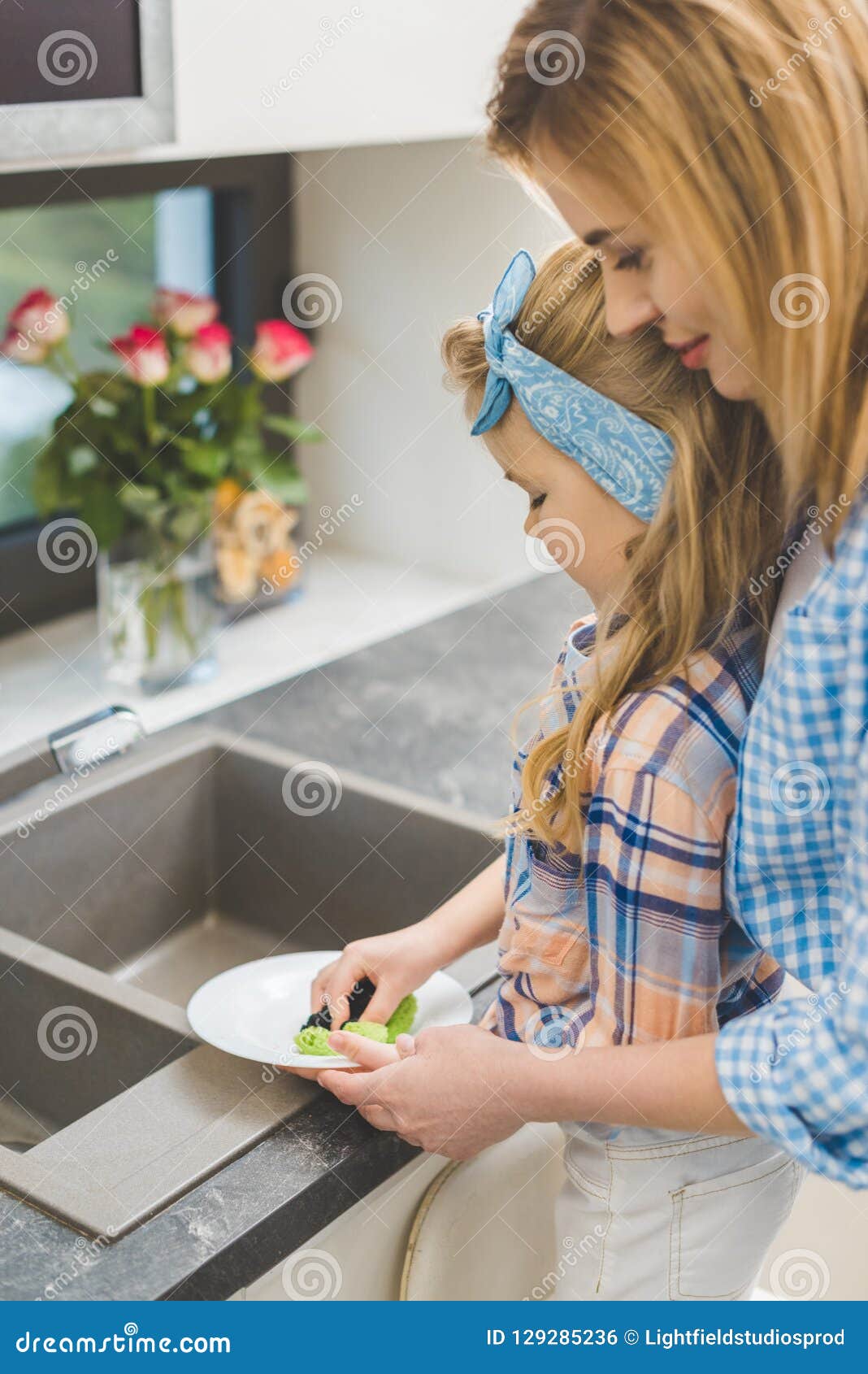 side view of little daughter helping mother to wash dishes after dinner