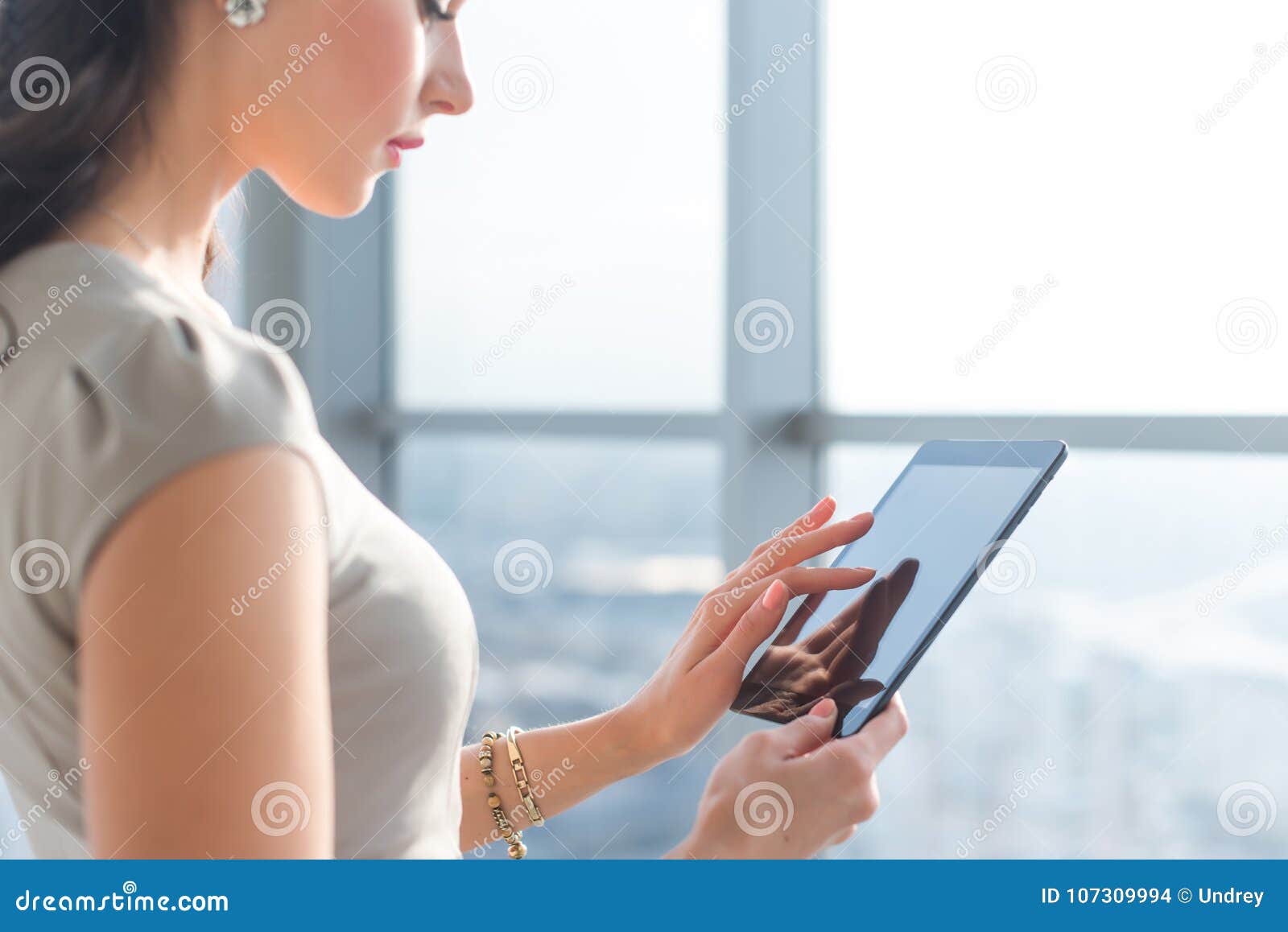 side view photo of young female teleworker using tablet, searching and browsing information via wi-fi connection