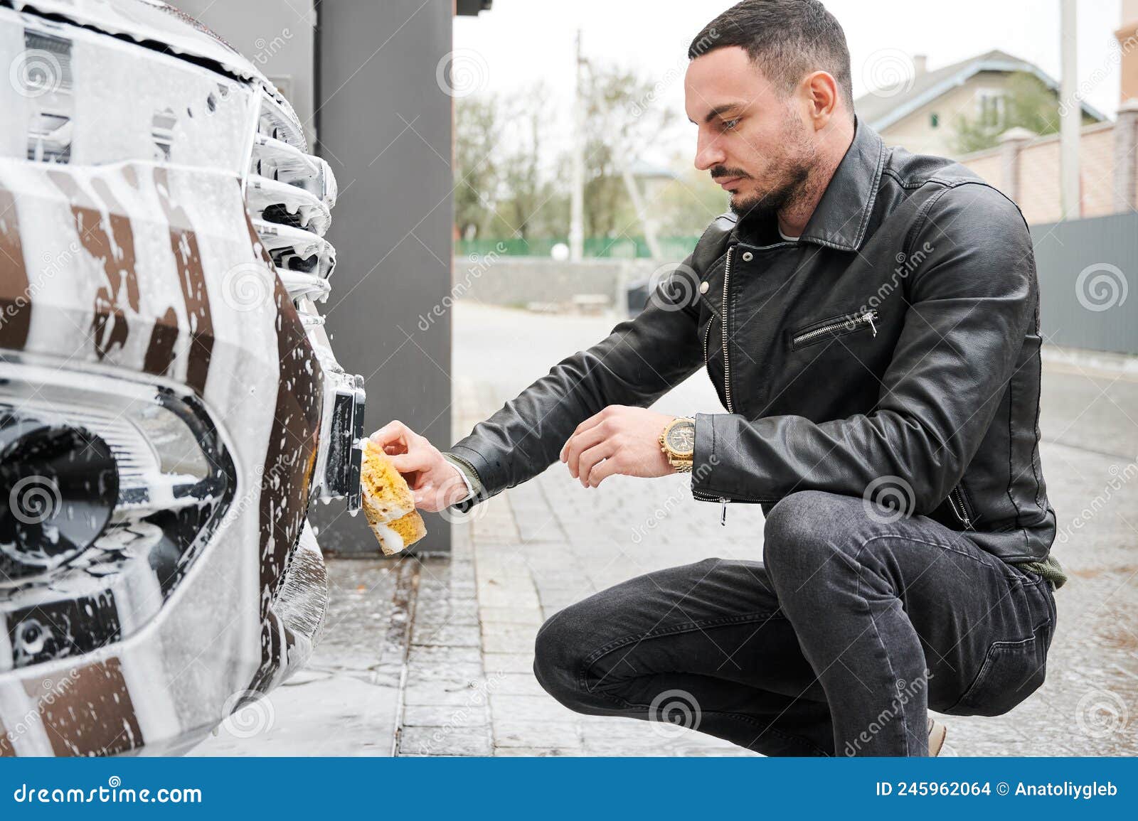 stylish man washing car with sponge on car wash.
