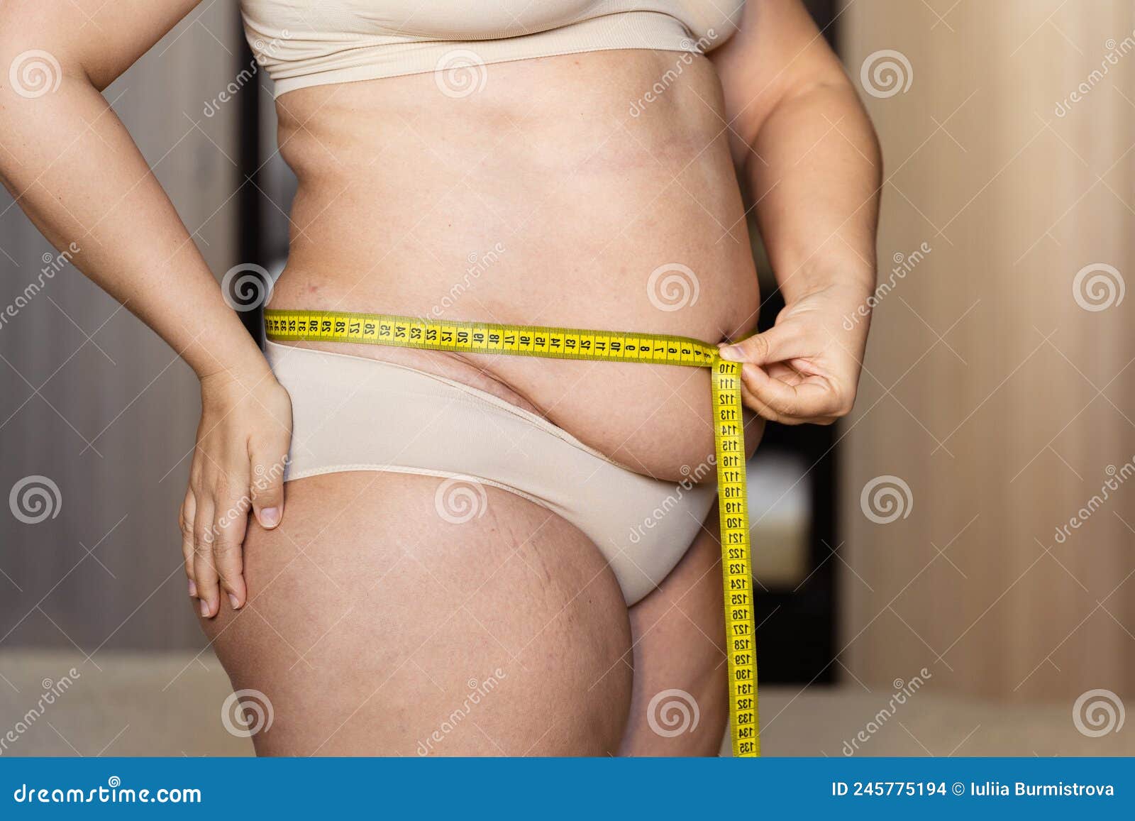 Back view of unrecognizable fat plump plus-size overweight woman standing  in beige bra, underpants near bed, showing squeezing excessive fat of back.  Body positive, obesity, weight loss, liposuction. Photos