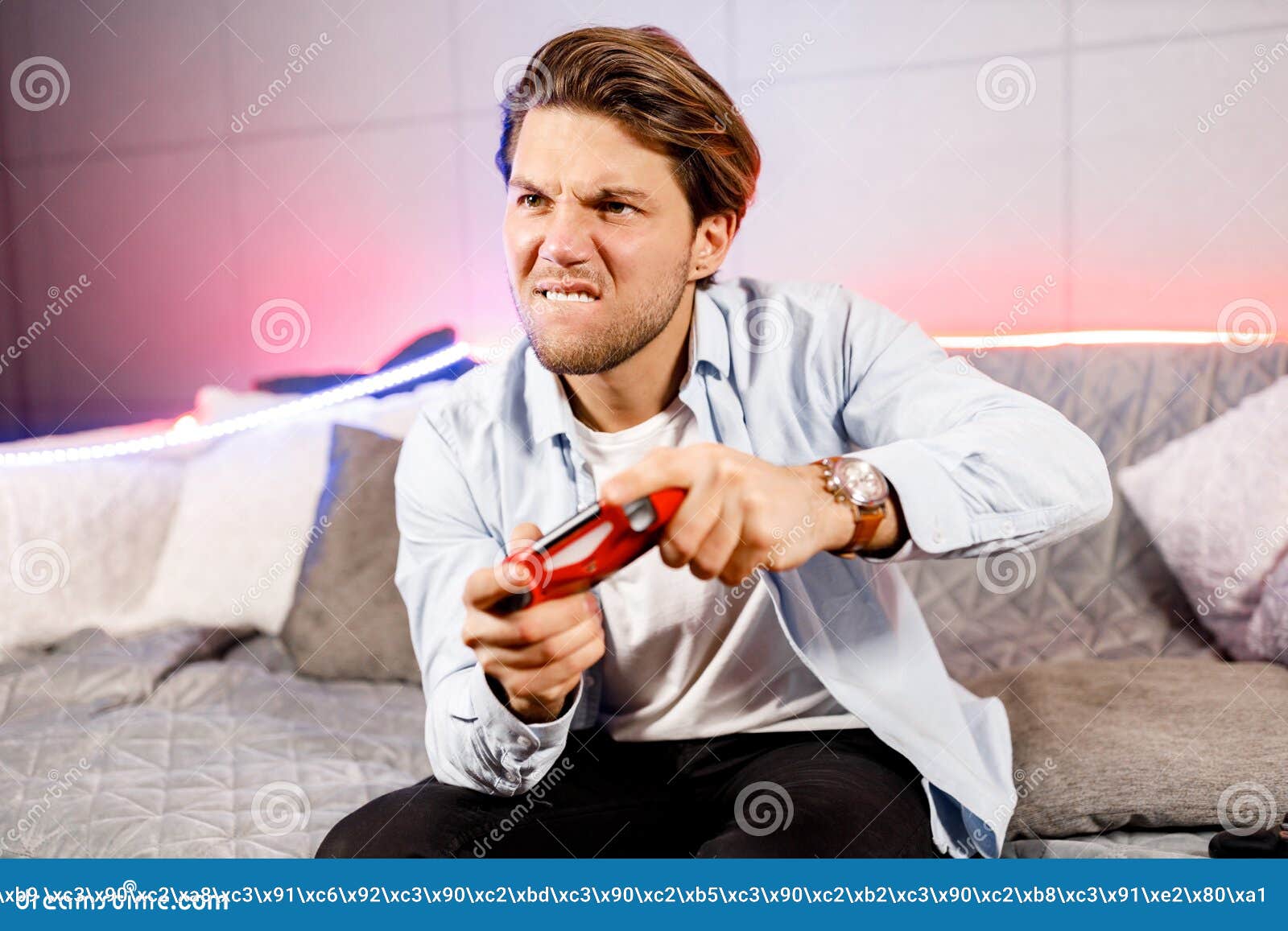 side view of venturous millennial male sit on neon sofa at home, having fun playing video games with red game pad