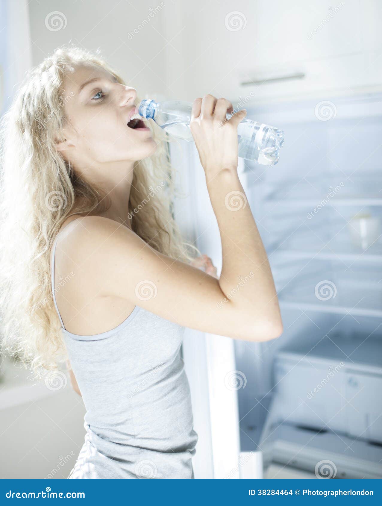 Side View of Young Woman Drinking Water from Bottle by Refrigerator