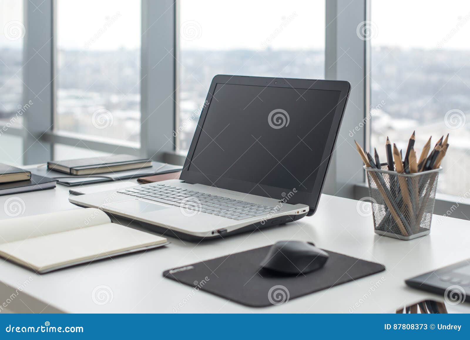 sideview of office desktop with blank laptop and various tools.