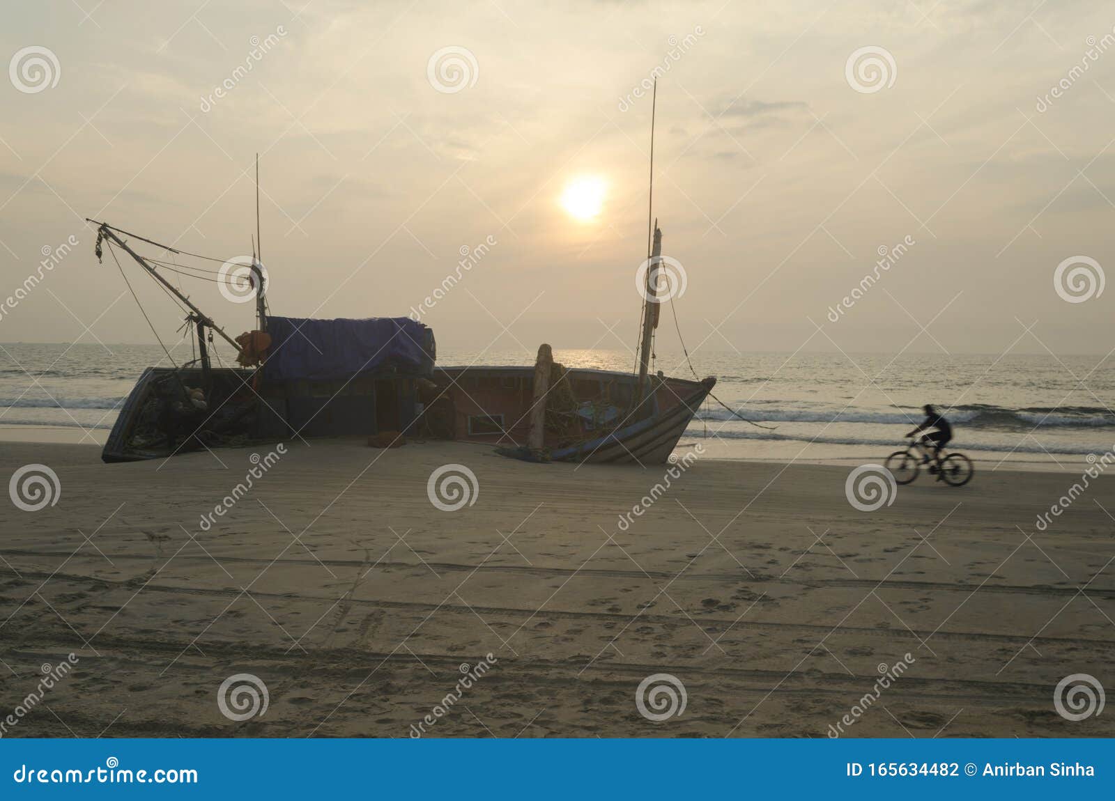 silhouette of a cyclist passing by a ship wreak on sunset beach