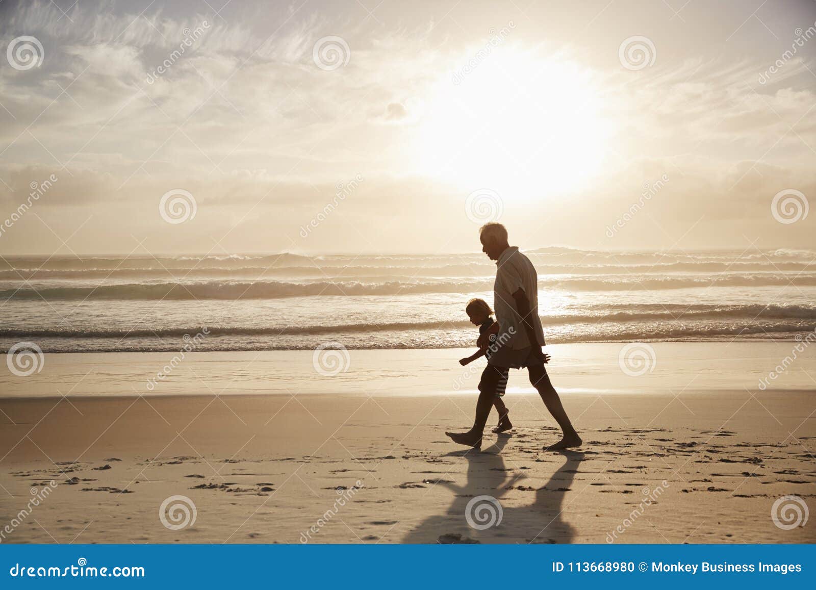 silhouette of grandfather walking along beach with grandson