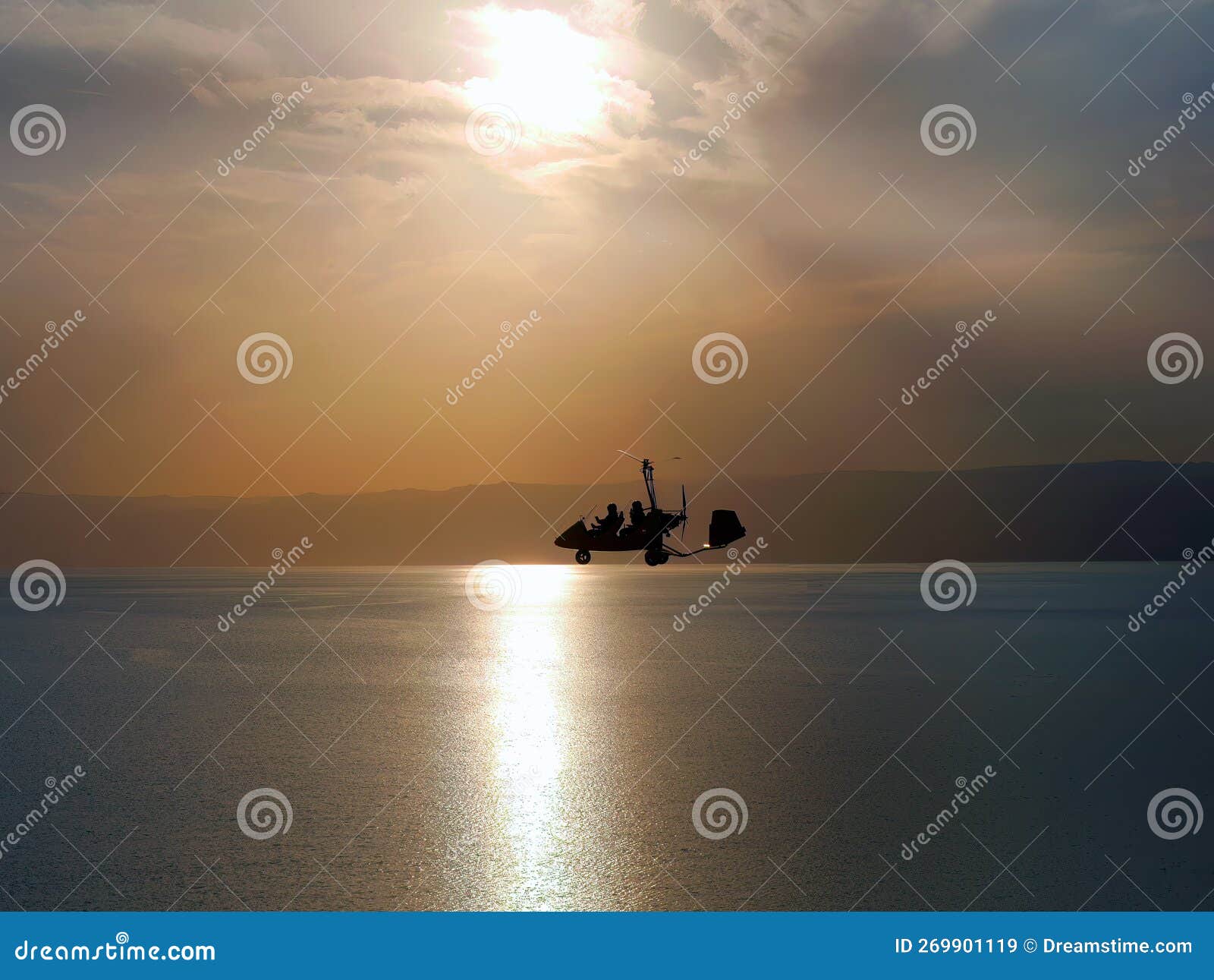 silhouette of gyrocopter, fun fly, aero sports, skydive, roto craft, gyroplane flying against sunset light over the dead sea,