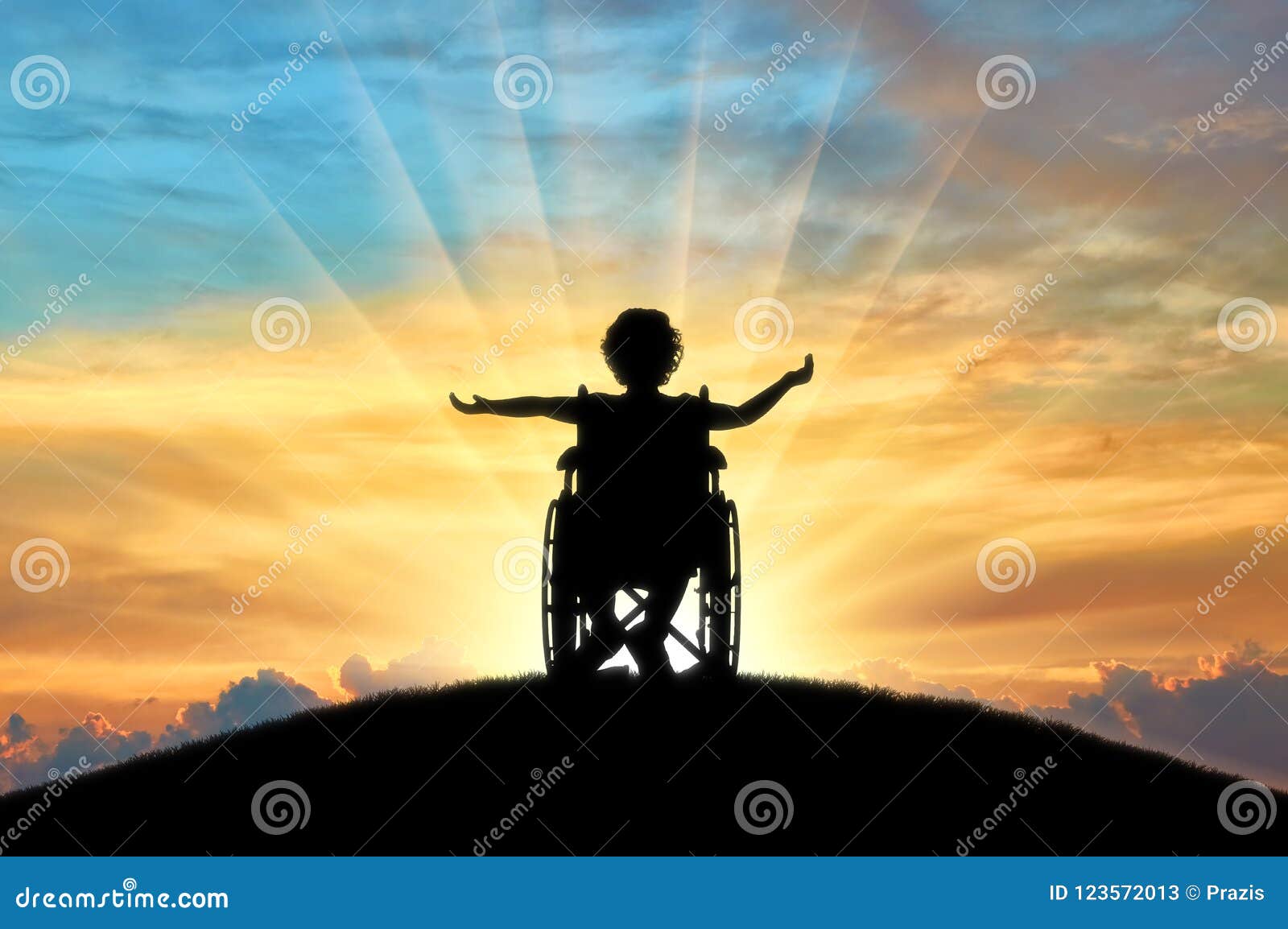 silhouette of a happy disabled child girl sitting in a wheelchair atop a hill at sunset