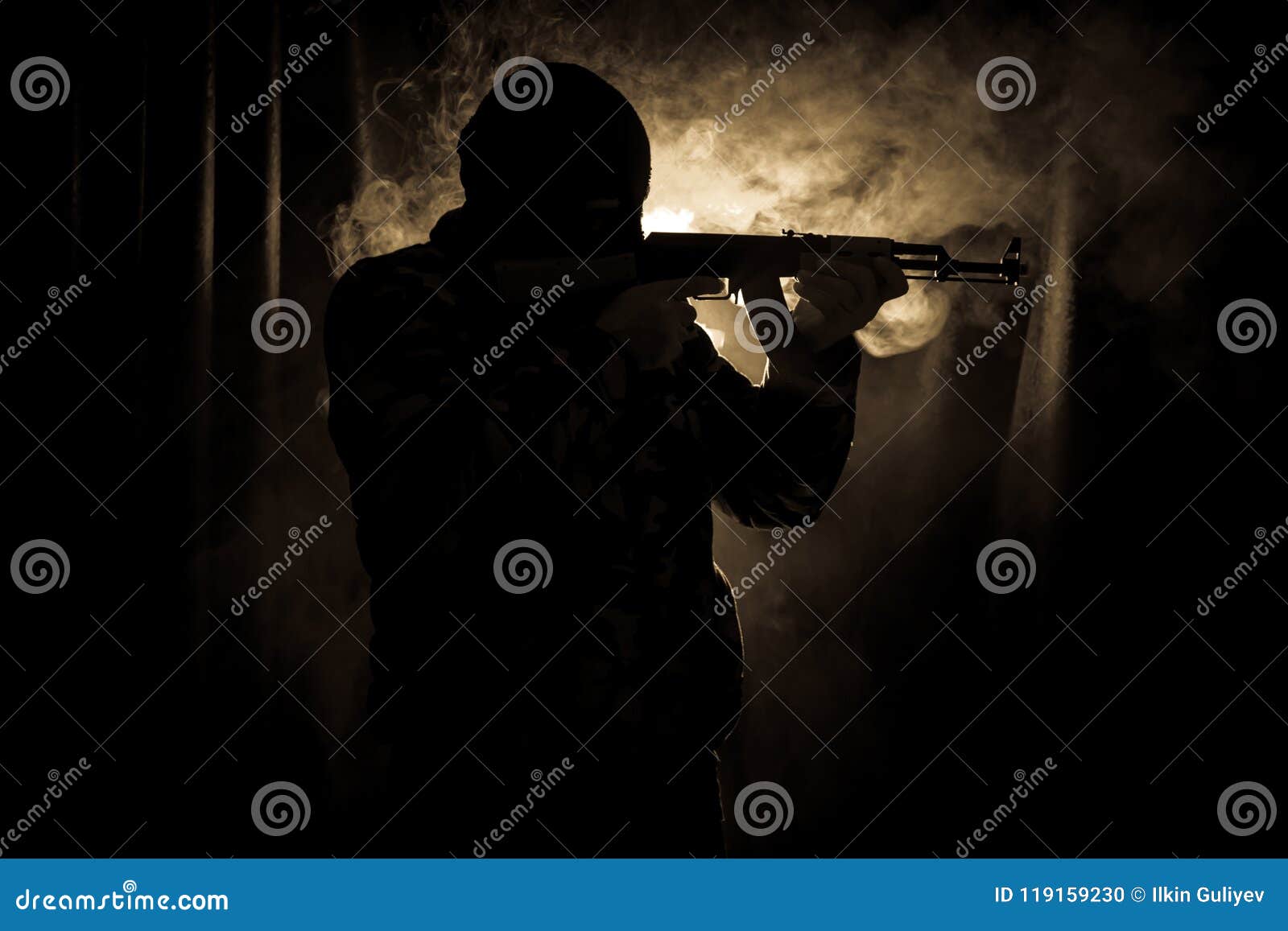 silhouette of man with assault rifle ready to attack on dark toned foggy background or dangerous bandit in black wearing balaclava