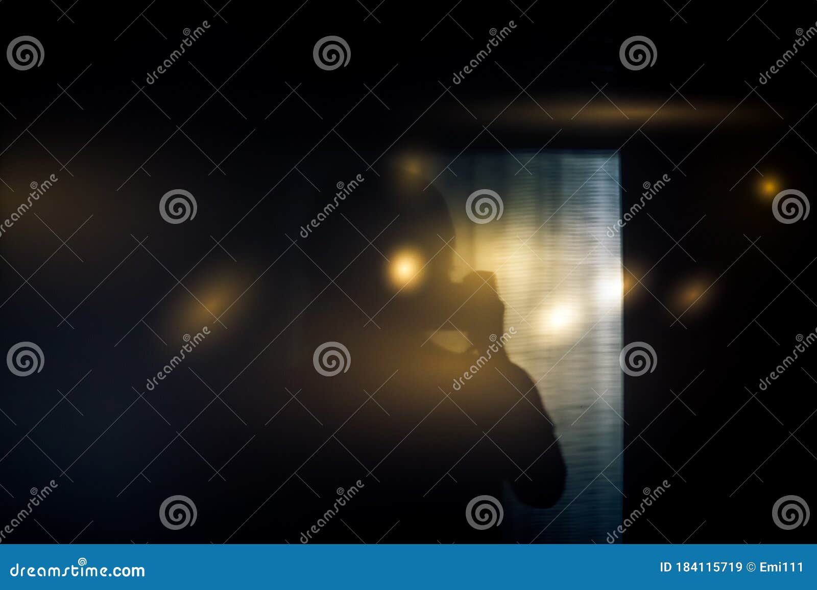 silhouette of  person holding camera in semi-darkness with sun flare in dark room in front of window