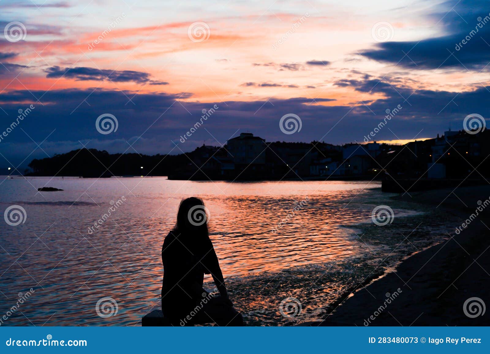 silhouette of a woman watching a beautiful view of a coast town on a sunset