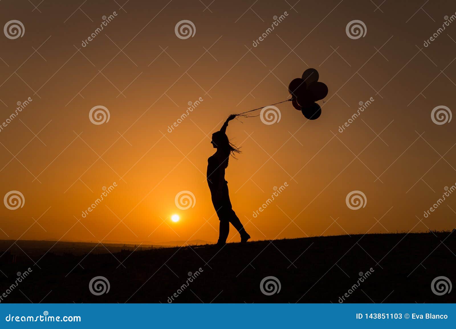 silhouette of a young woman playing with balloons at sunset