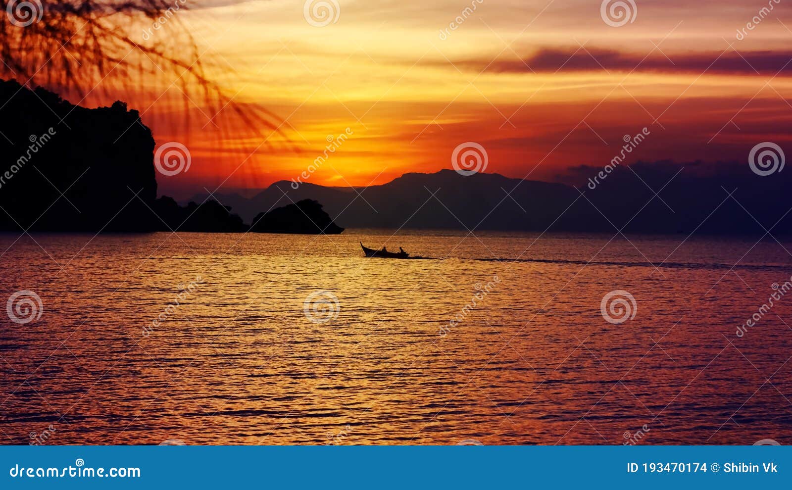 sillhoute of two peoples in a boat with a beautiful setting sun behind the hills and rocks with its reflection over the sea waves