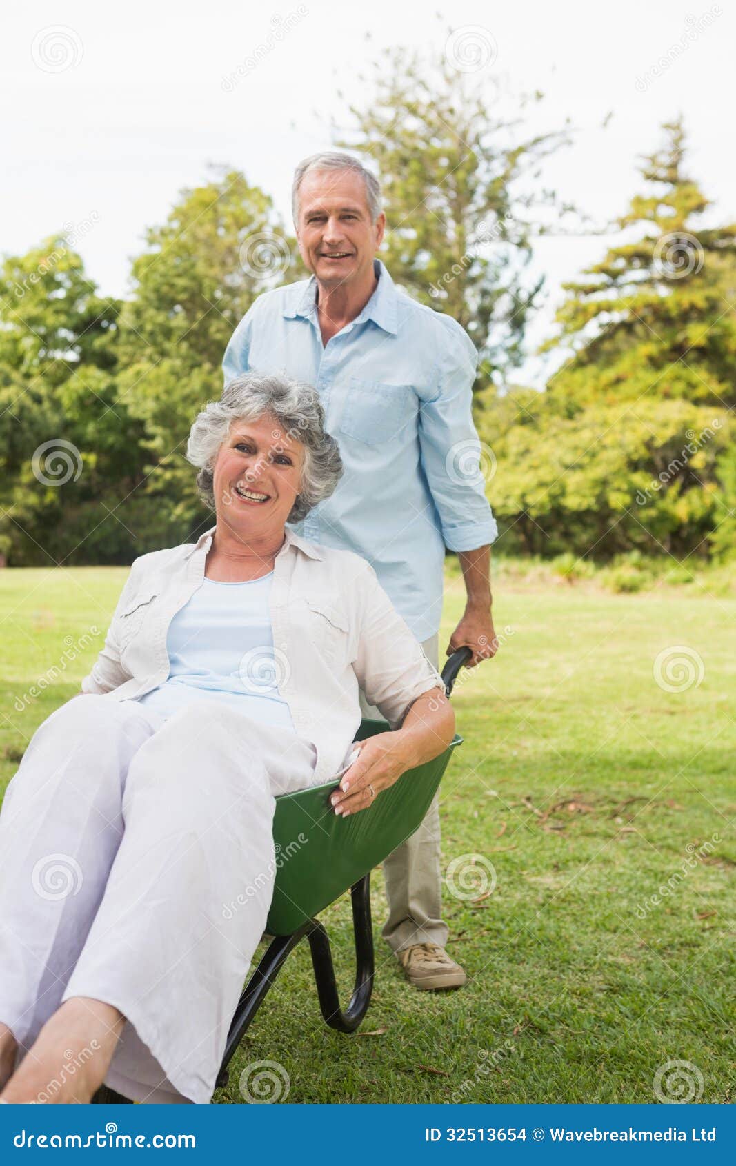 Silly man pushing his wife in a wheelbarrow. Silly men pushing his wife in a wheelbarrow outside in the sunshine