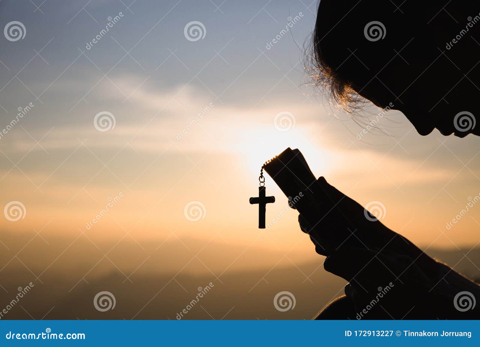 siluette of christian woman  holding a bible and wooden christian cross necklace while praying to god