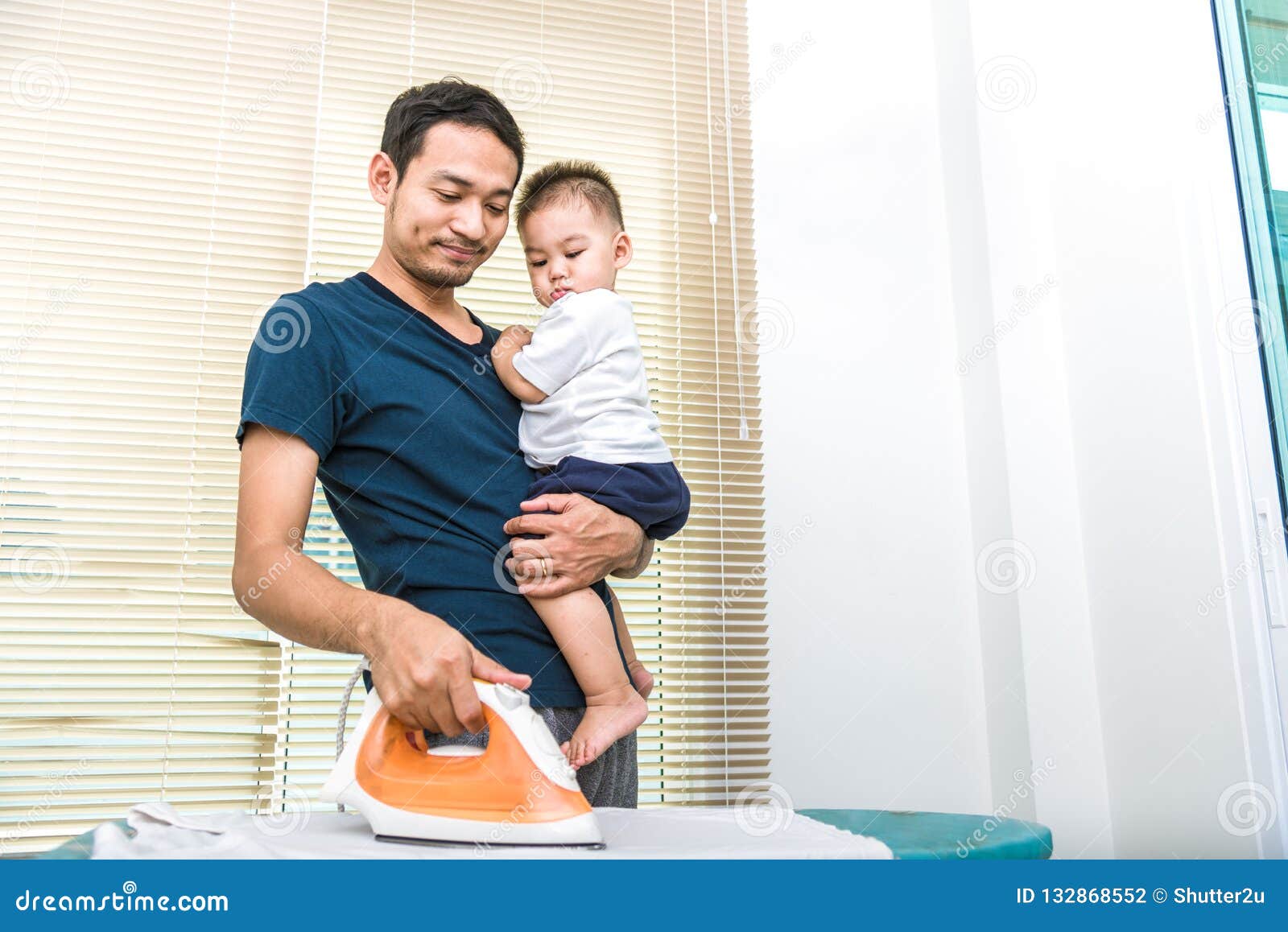 single dad is ironing while carrying his son. people and lifestyles concept.