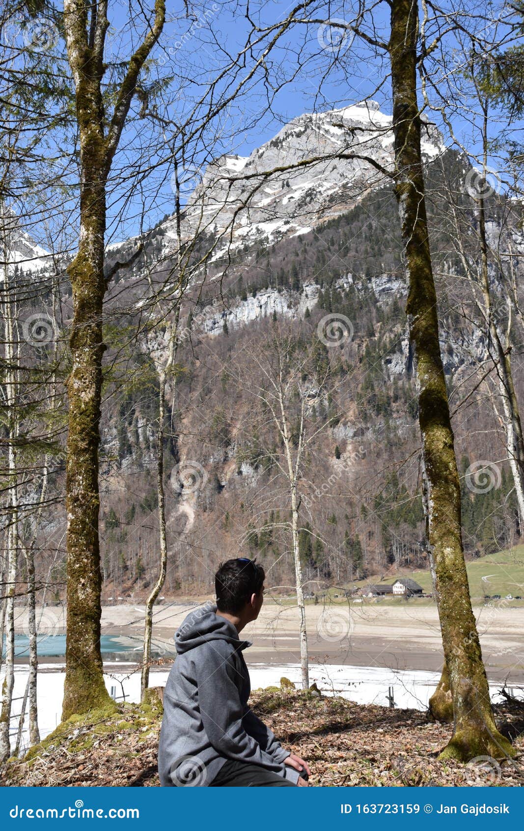 a sitting boy between conifer trees observing klÃÂ¶ntalersee lake in early spring sunny day in klÃÂ¶ntal