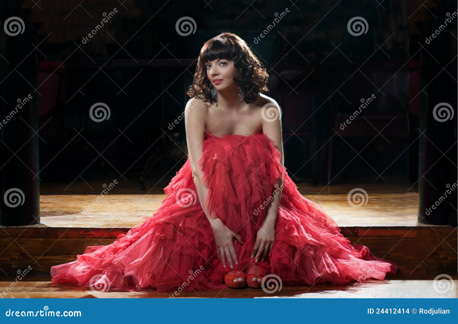 Sitting woman in red evening dress against the dark background