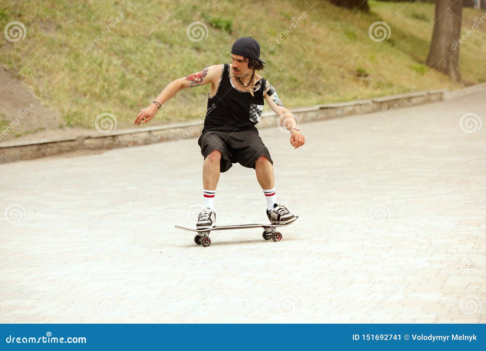 Skateboarder som cloudly gör ett trick på stadens gata i dag Ung man i gymnastikskor och lock som rider och longboarding på asfalten Begrepp av fritidsaktivitet, sporten, ytterligheten, hobbyen och rörelse