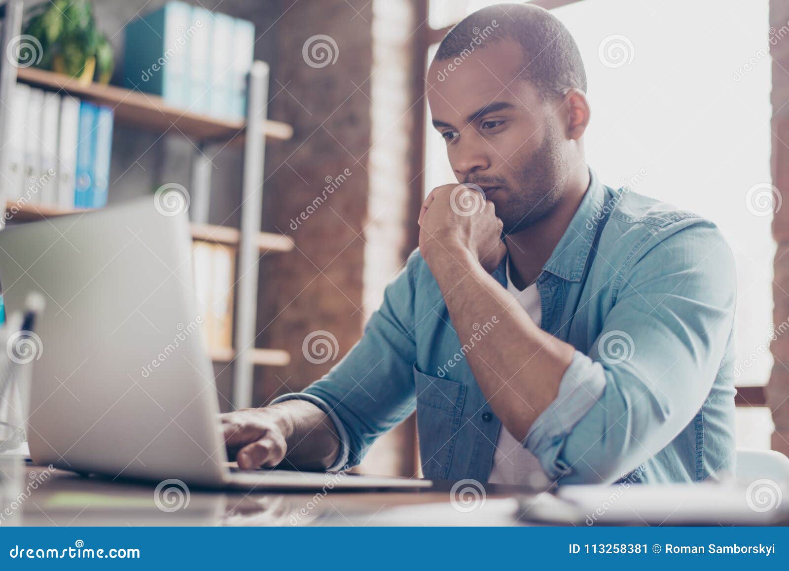 skeptic young afro freelancer is making decision sitting at the office in casual smart, analyzing the data in the computer