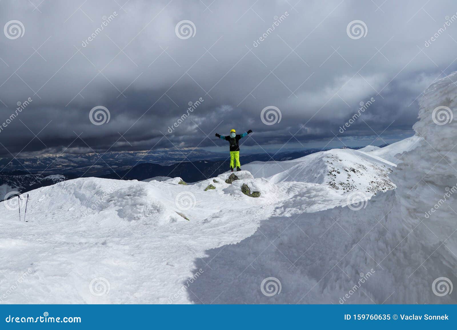 skier-athlete stands on the edge of a high cliff against high tatras and approaching thunderstorm. enjoys view to the valley and