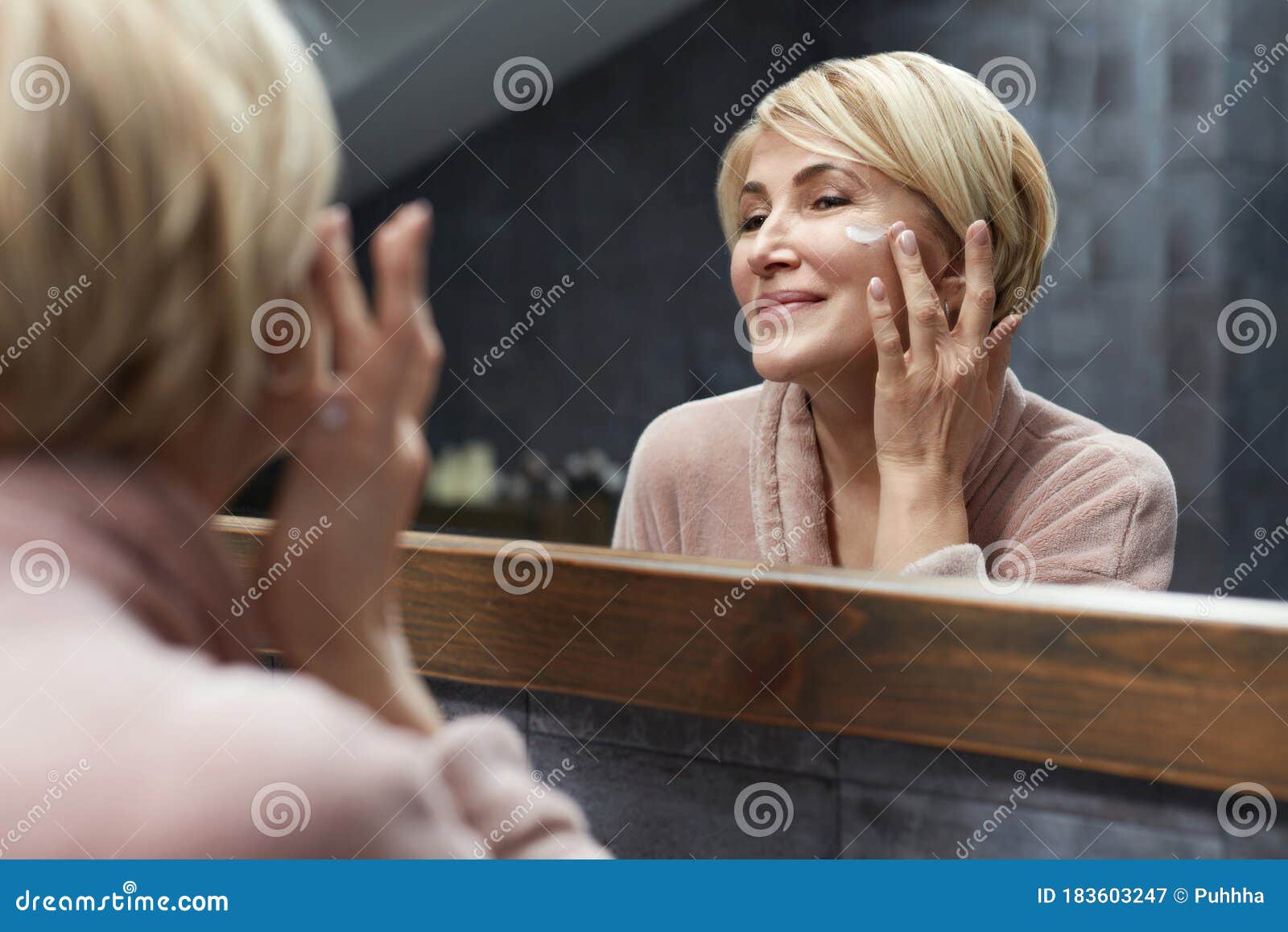 skincare routine. mature woman uses cosmetic cream on face skin in front of the mirror reflection.