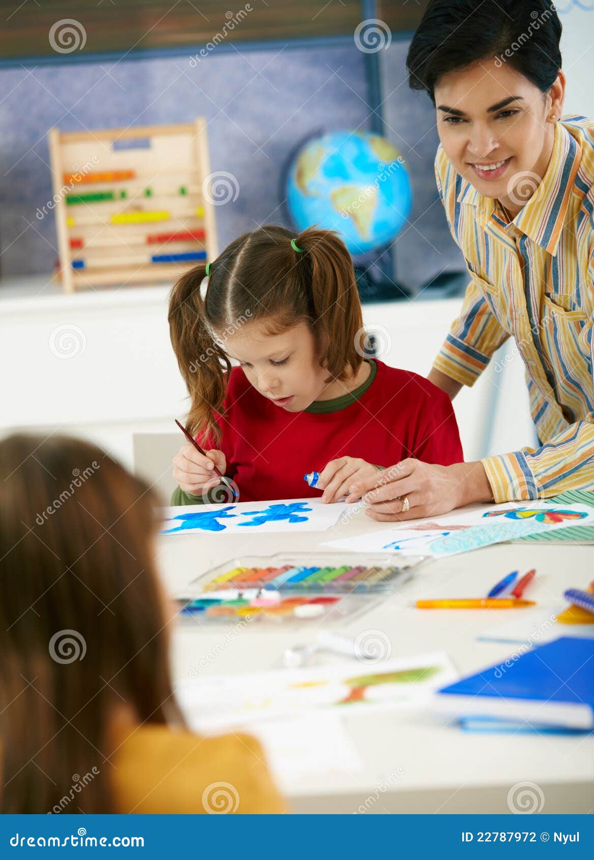 Skolabarn och lärare i konstgrupp. Elementära ålderbarn som sitter runt om skrivbordet som tycker om målningen med färger i konstgrupp i grundskola för barn mellan 5 och 11 årklassrum.