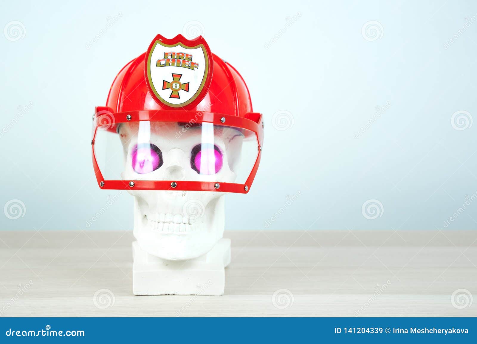 Skull sculpture wearing a red helmet and bright pink eyes. Copy space.