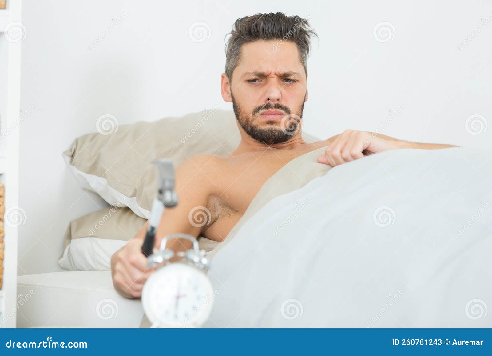 sleepy young man breaking alarm with hammer