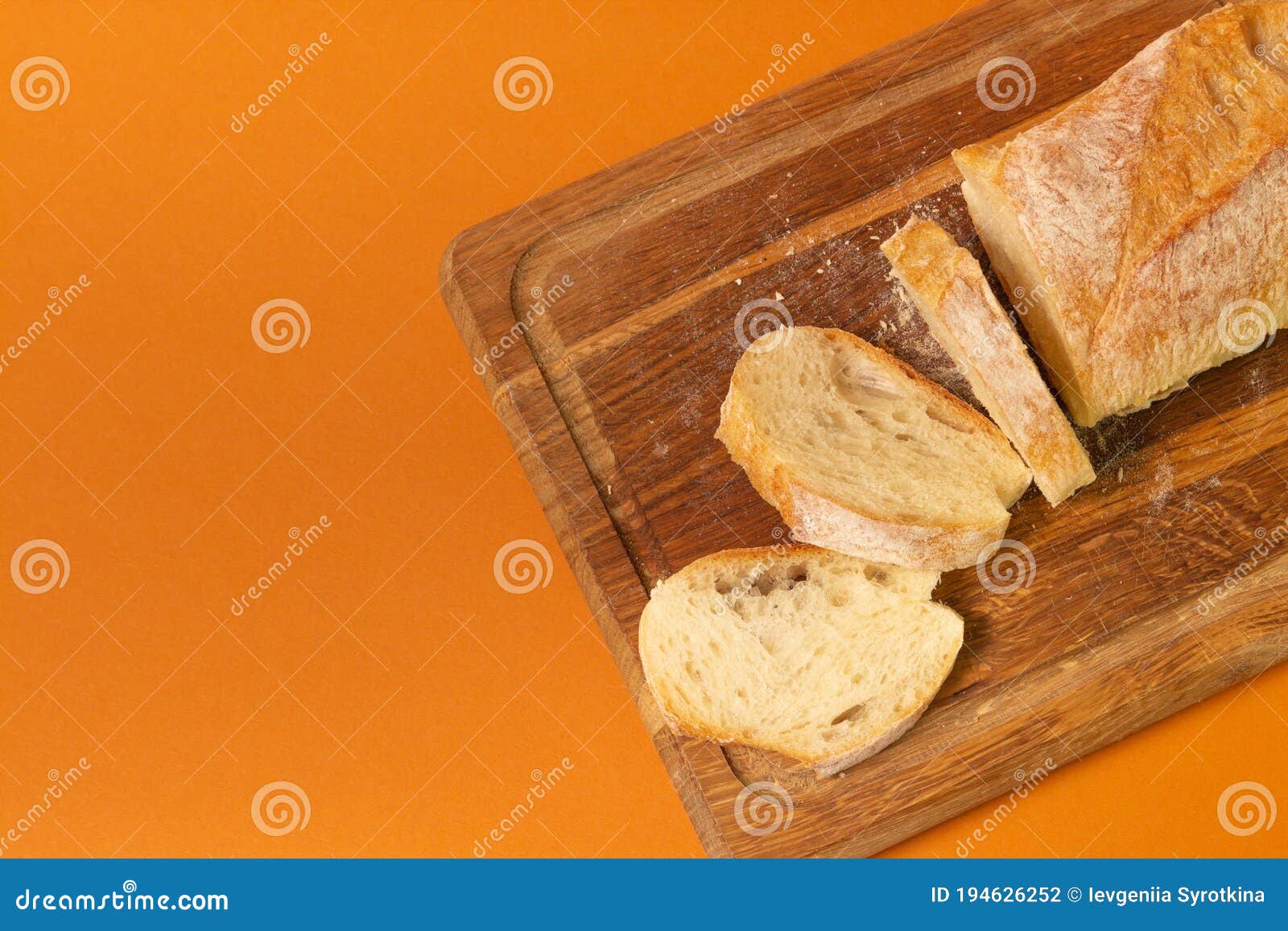 sliced bread baguette on a wooden cutting board on a terracote color background. close-up high quality photo
