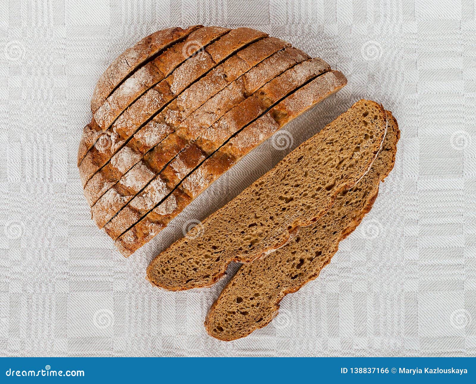 sliced round loaf of rye bread with an appetizing crispy brown crust on a gray linen tablecloth. tasty, usefull and nutritious.