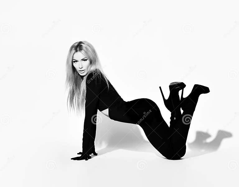 Slim Blonde Woman With Pouty Lips In Tight Black Overall Suit And High Heeled Shoes Stands On