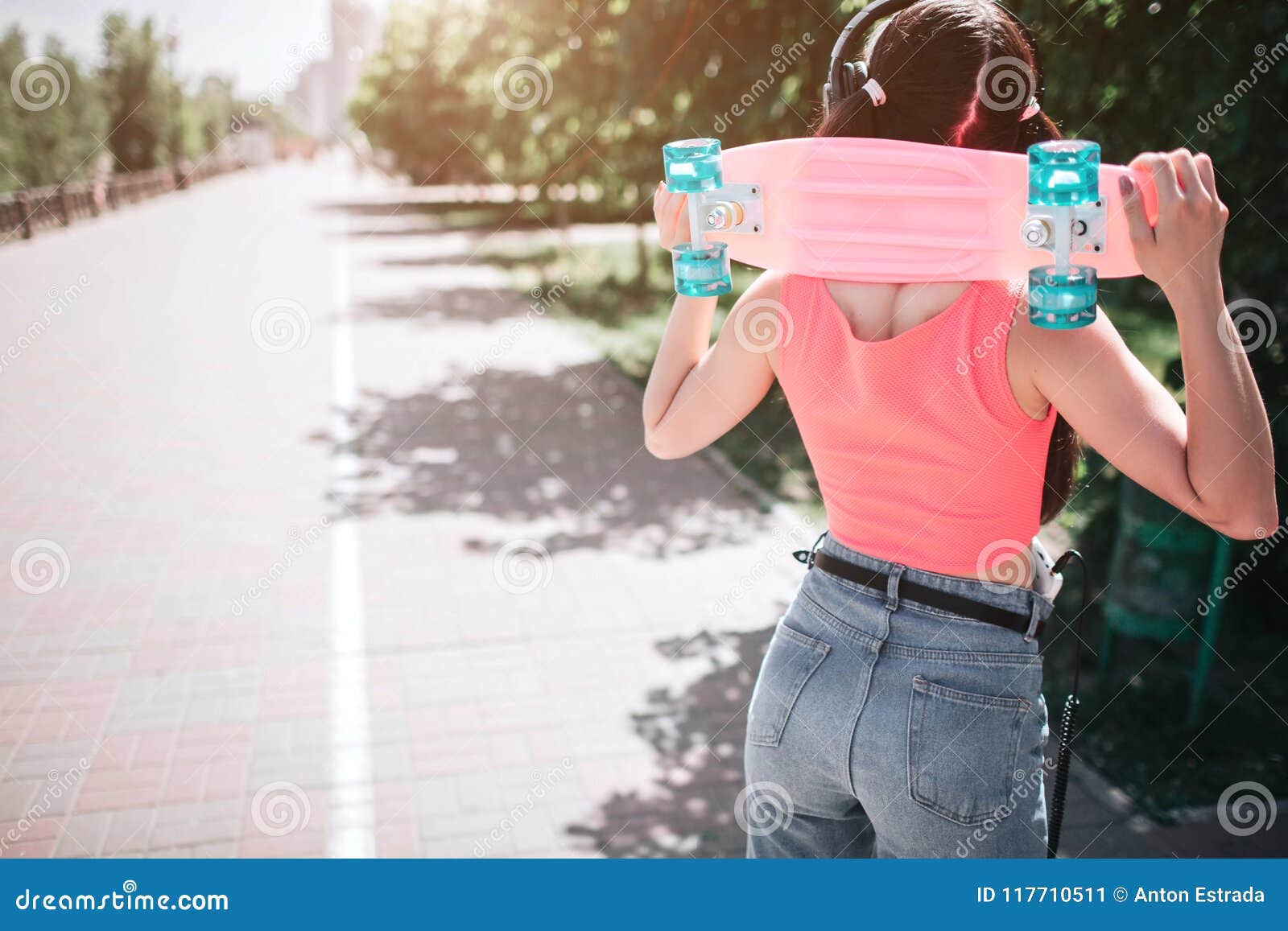 slim and well-built melomaniac girl is posing. she is standing back to camera and holding skate on the neck. she has
