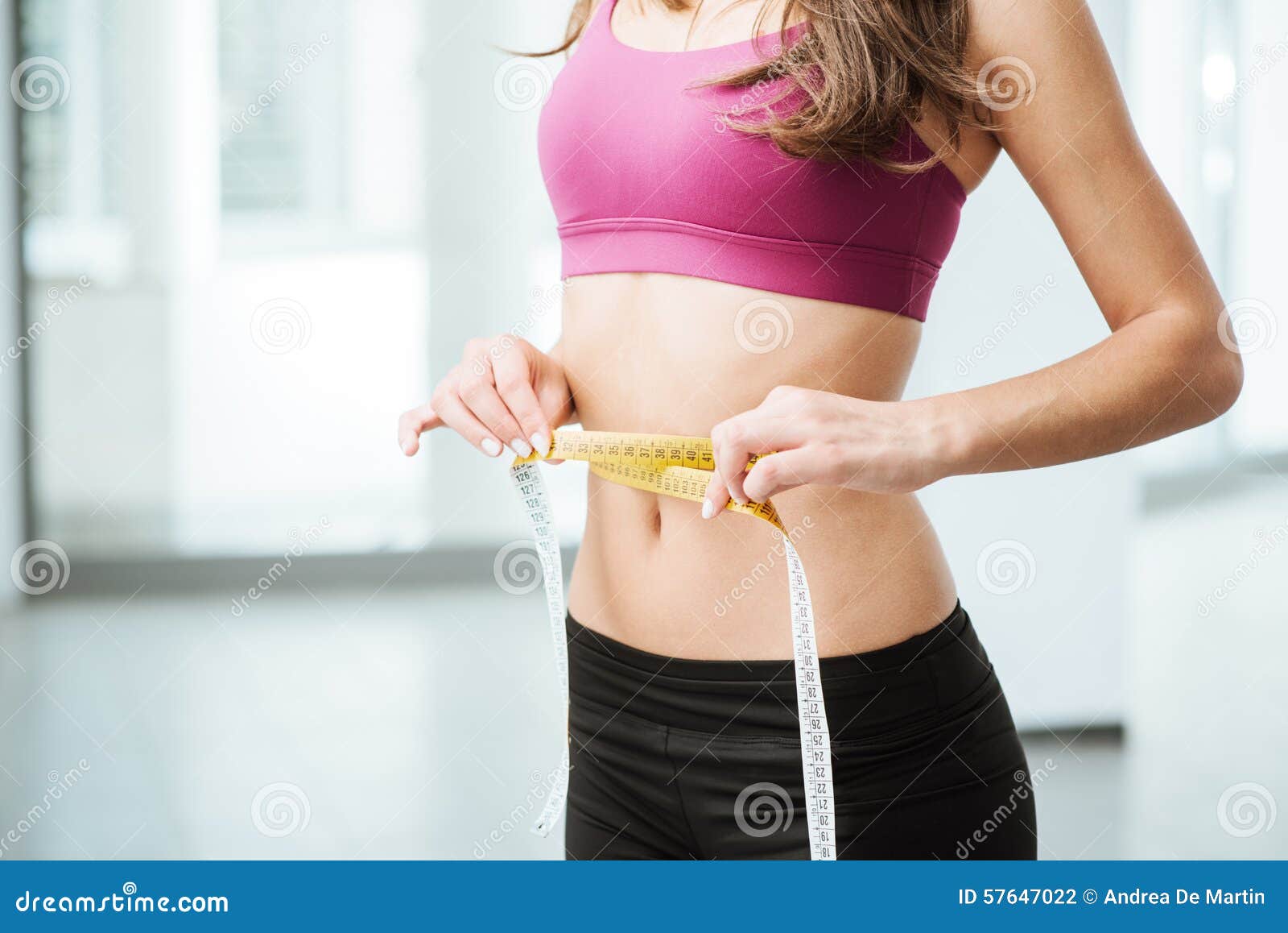 Photo of Young slim woman measuring her waist with a tape