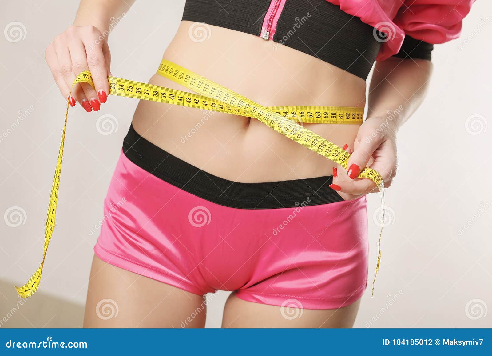 Photo of Young slim woman measuring her waist with a tape