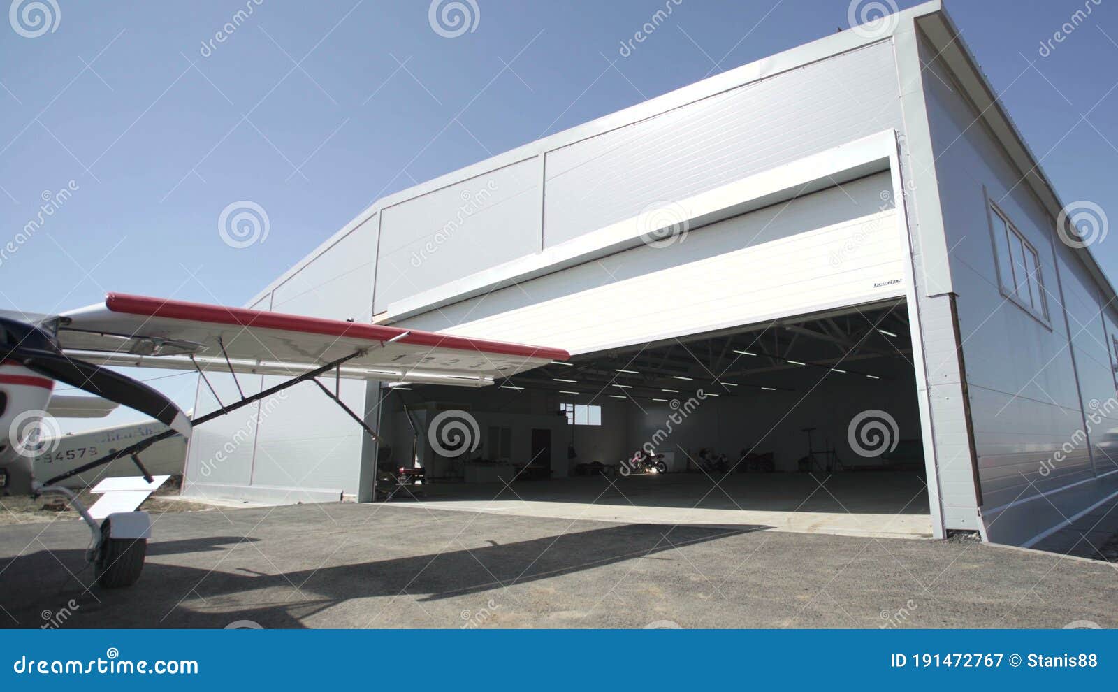 small airplanes outside hangar. door is opening. visible part of a small aircraft