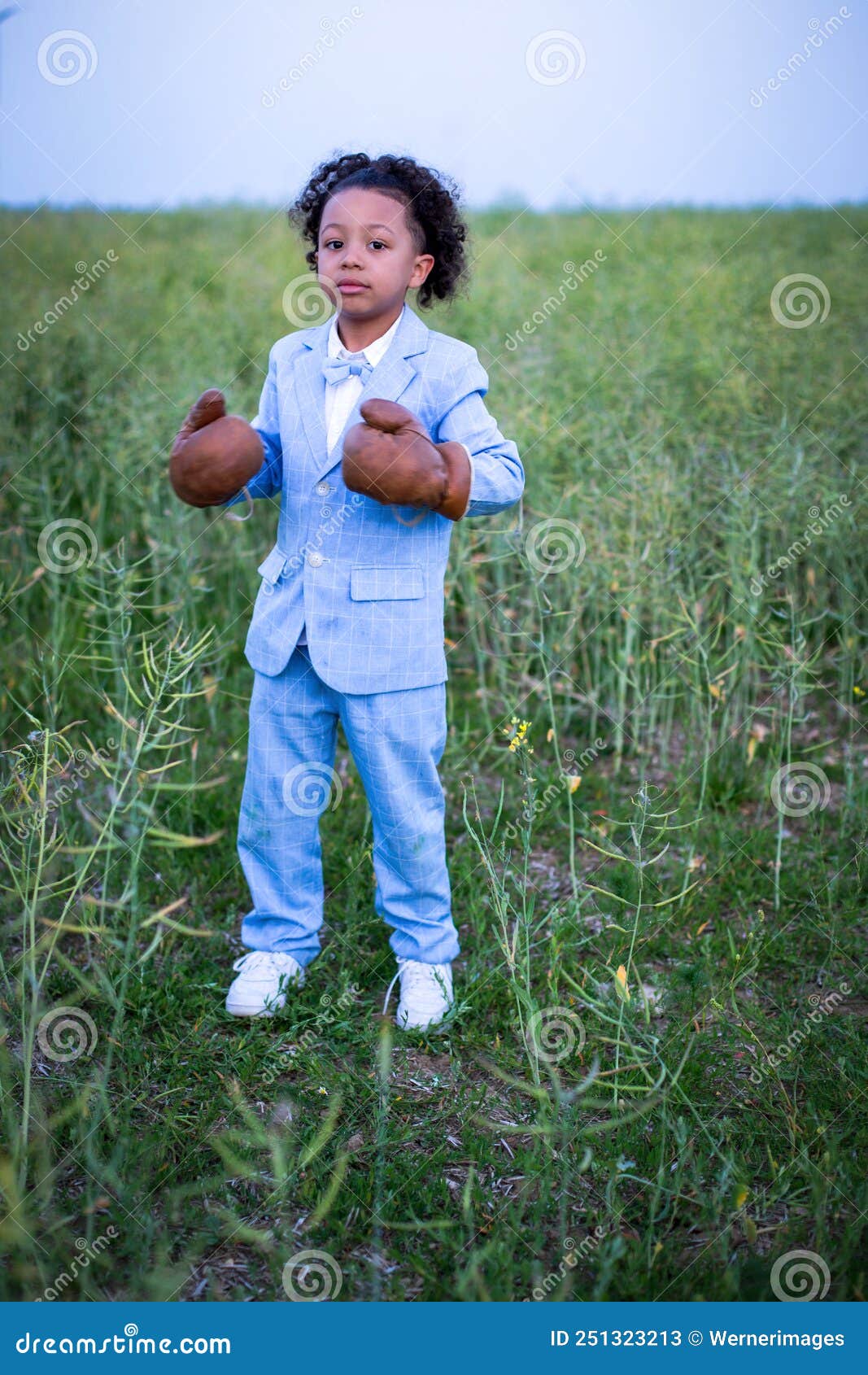Small Black Boy in Blue Suit with Boxing Gloves Standing in a Field
