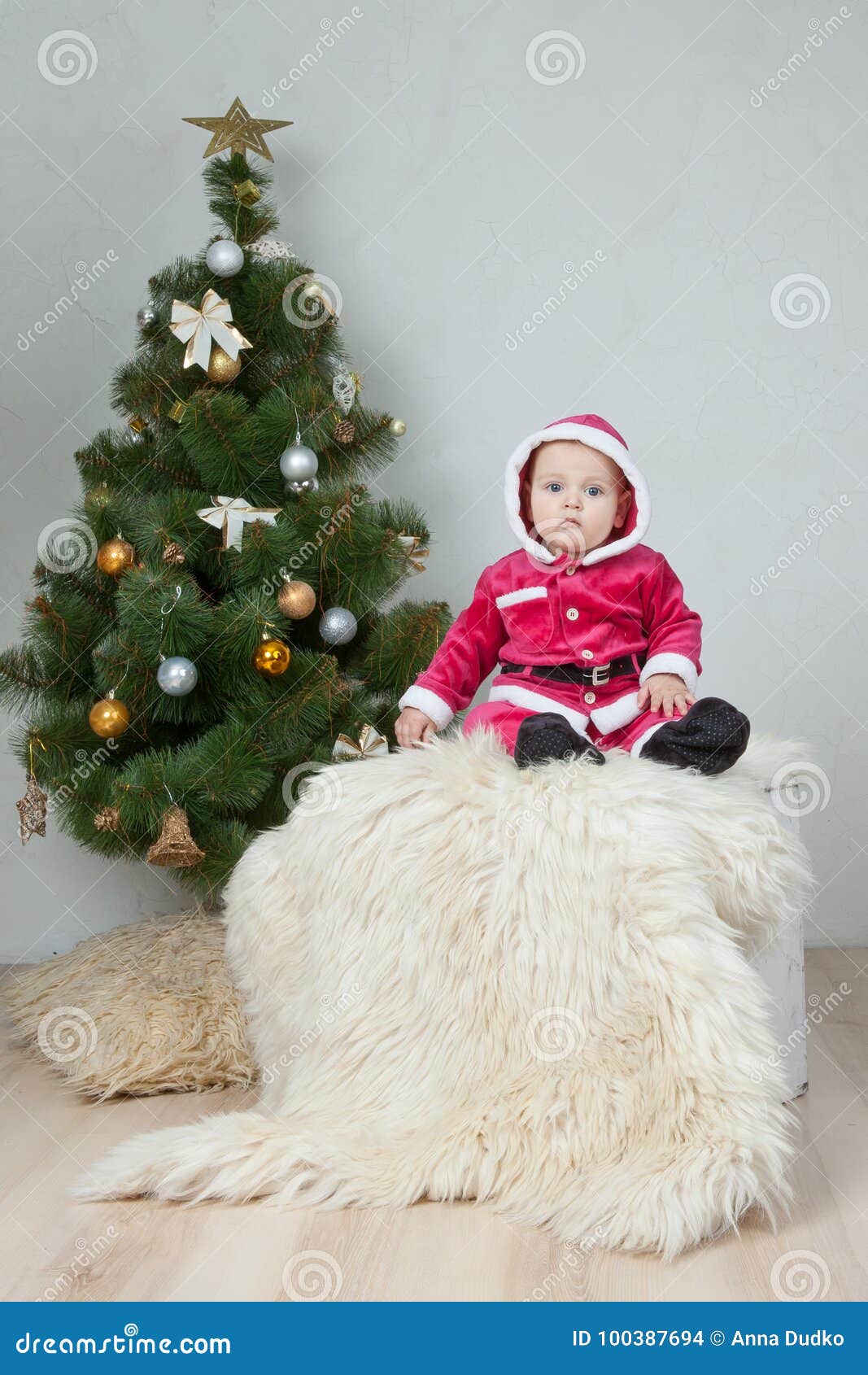 Small boy in Santa suit plays near new-year tree in white studio.