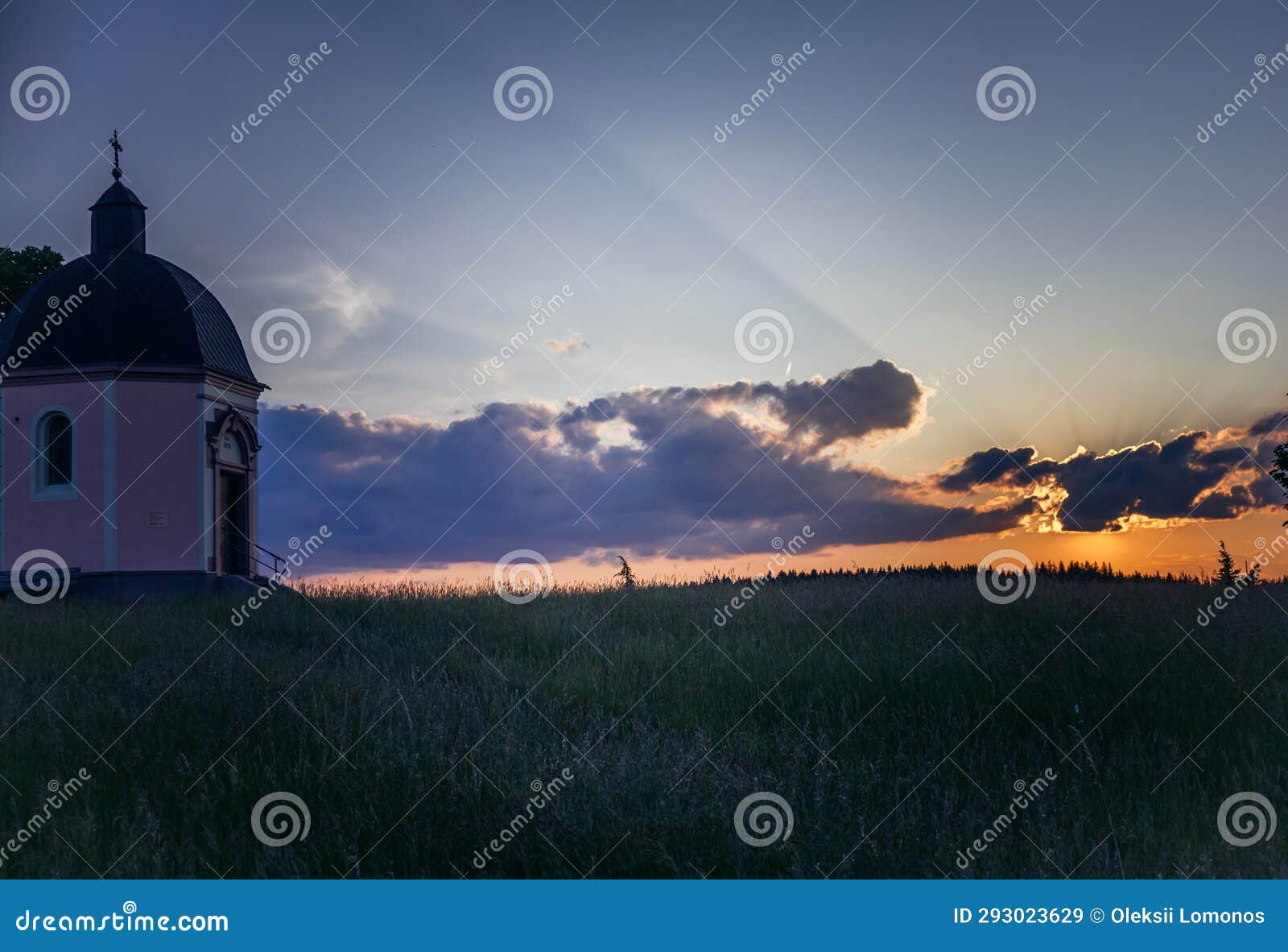 a small building in a field with a sky background and clouds in the background with sun rays coming through