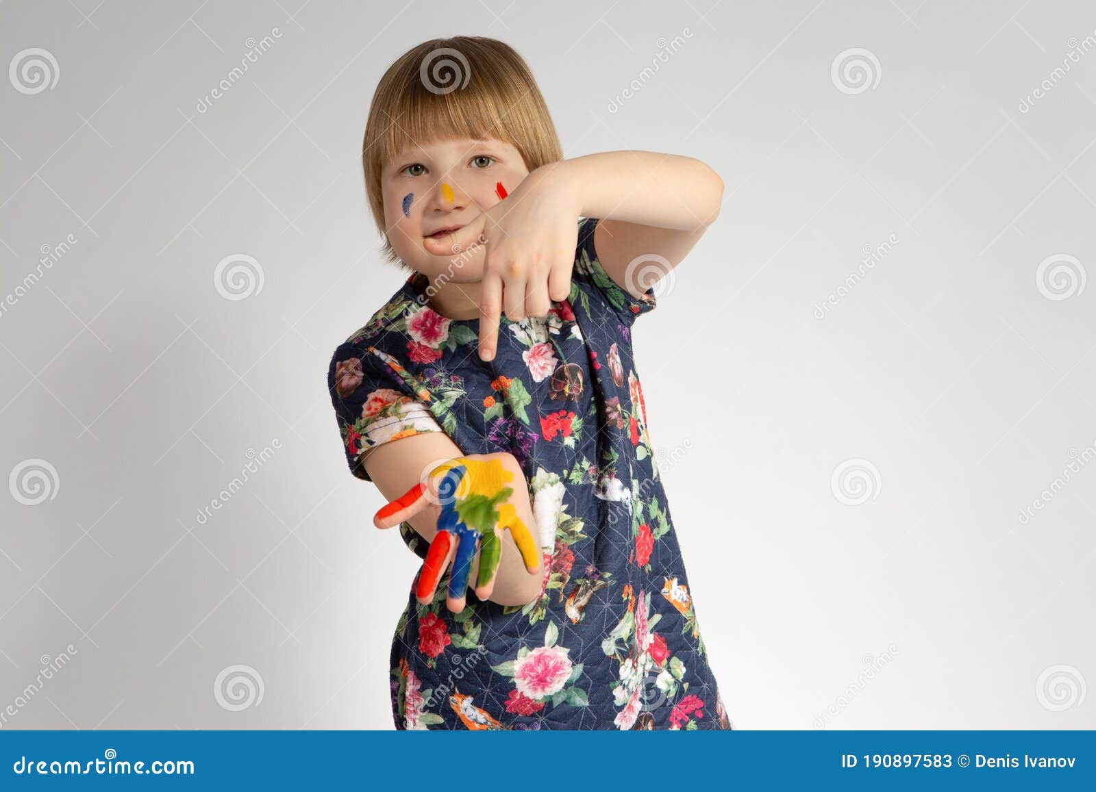 a small cheerful smiling girl shows index finger at leftist hands that she got dirty in facial paint