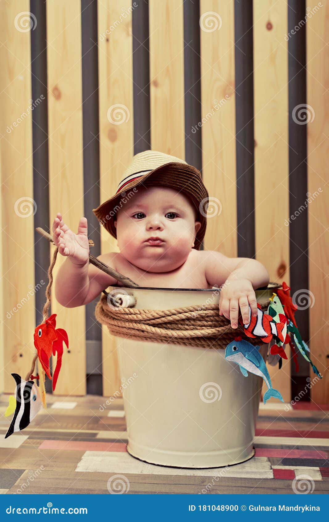 A Small Child in a Straw Hat Sits in a Bucket with a Fishing Rod