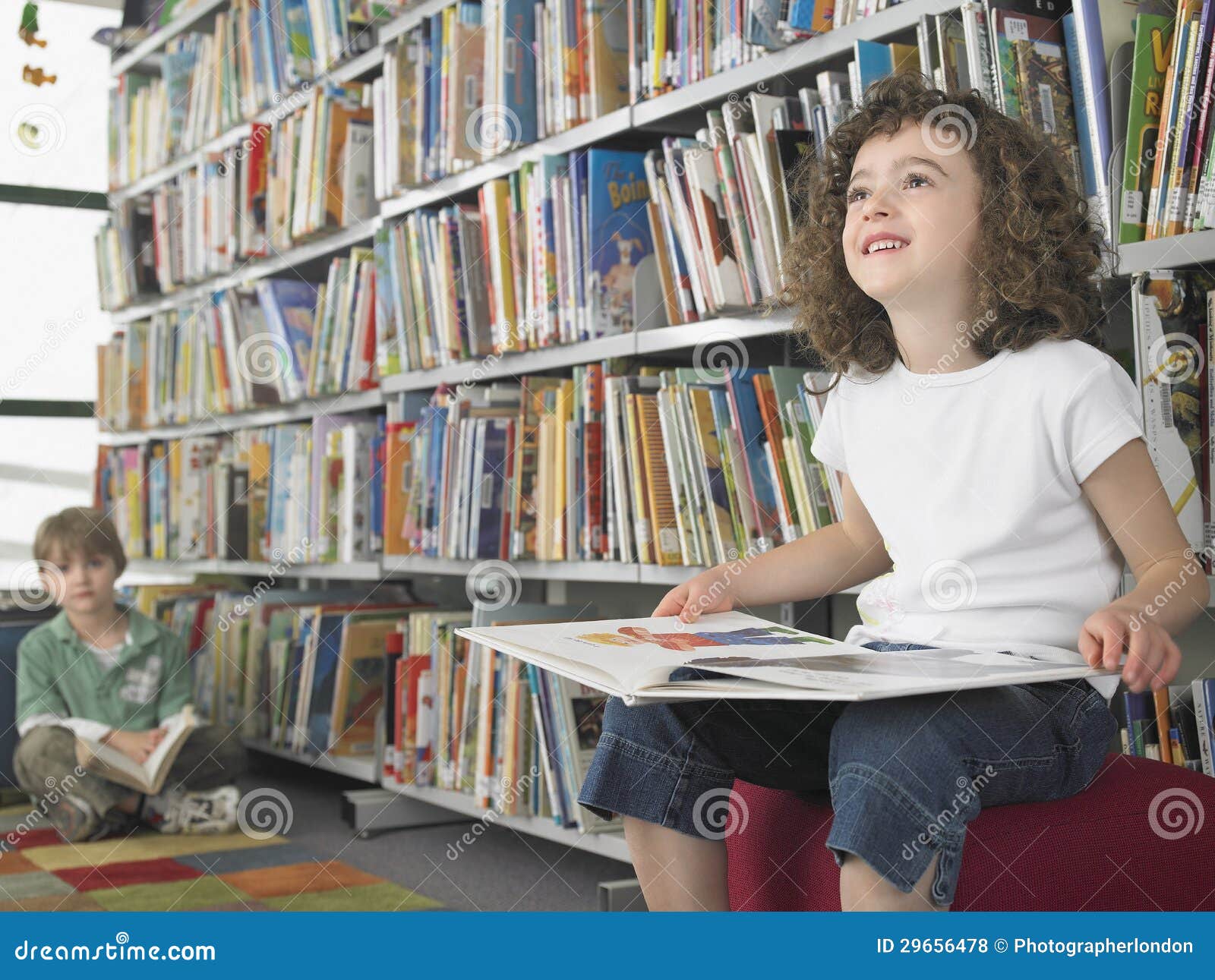 Small girl reading book with boy in background