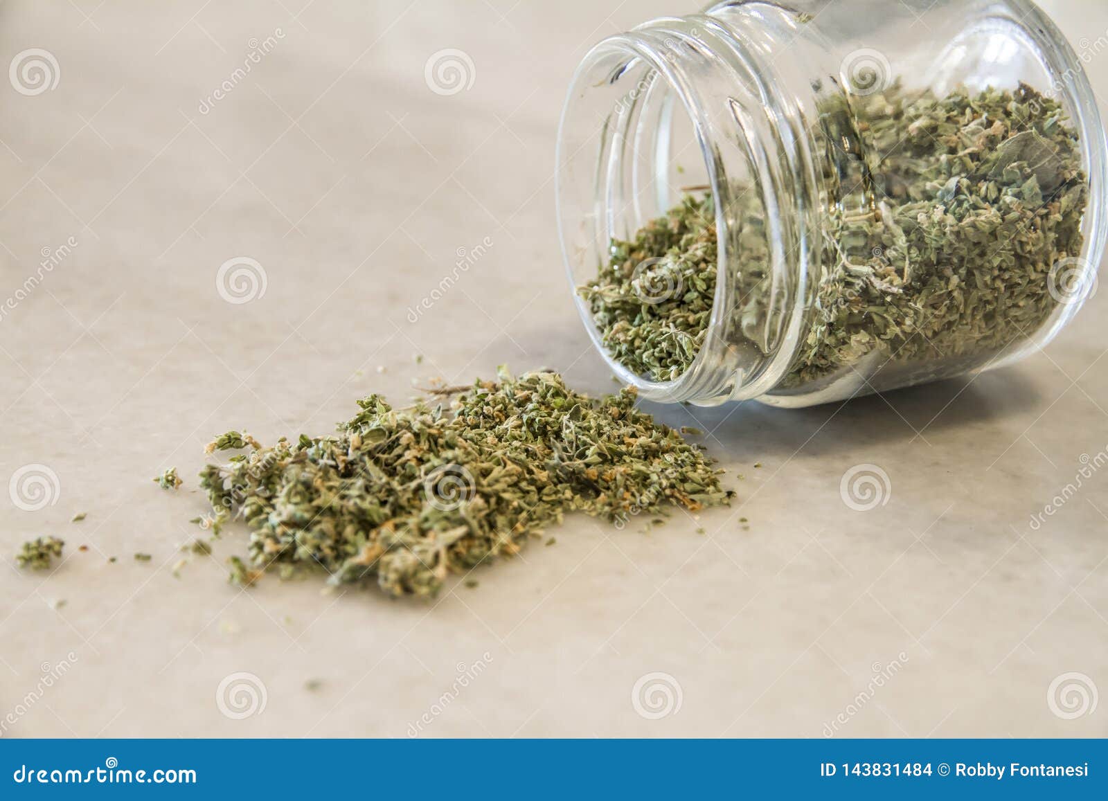 Small Jar of Dried Oregano Spilled on a Marble Top with Selective Focus