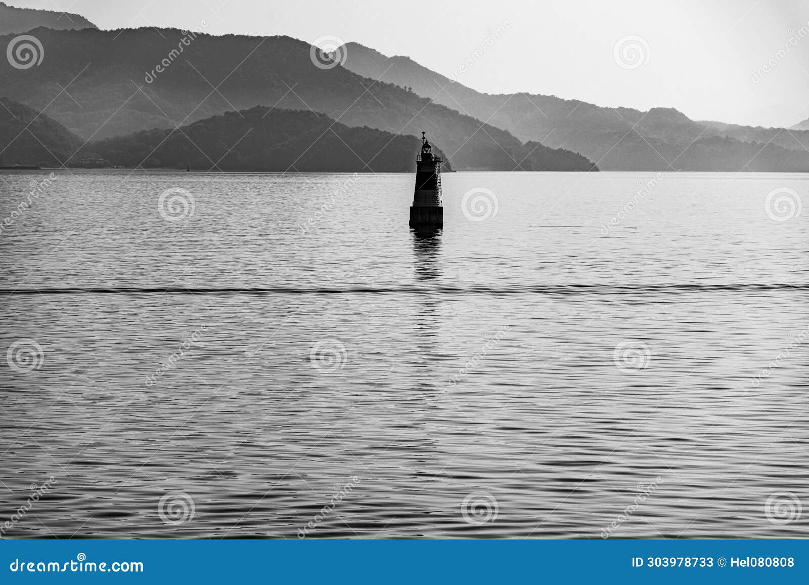 small lighthouse on japanese seto inland sea with foggy mountains in background. black and white photo