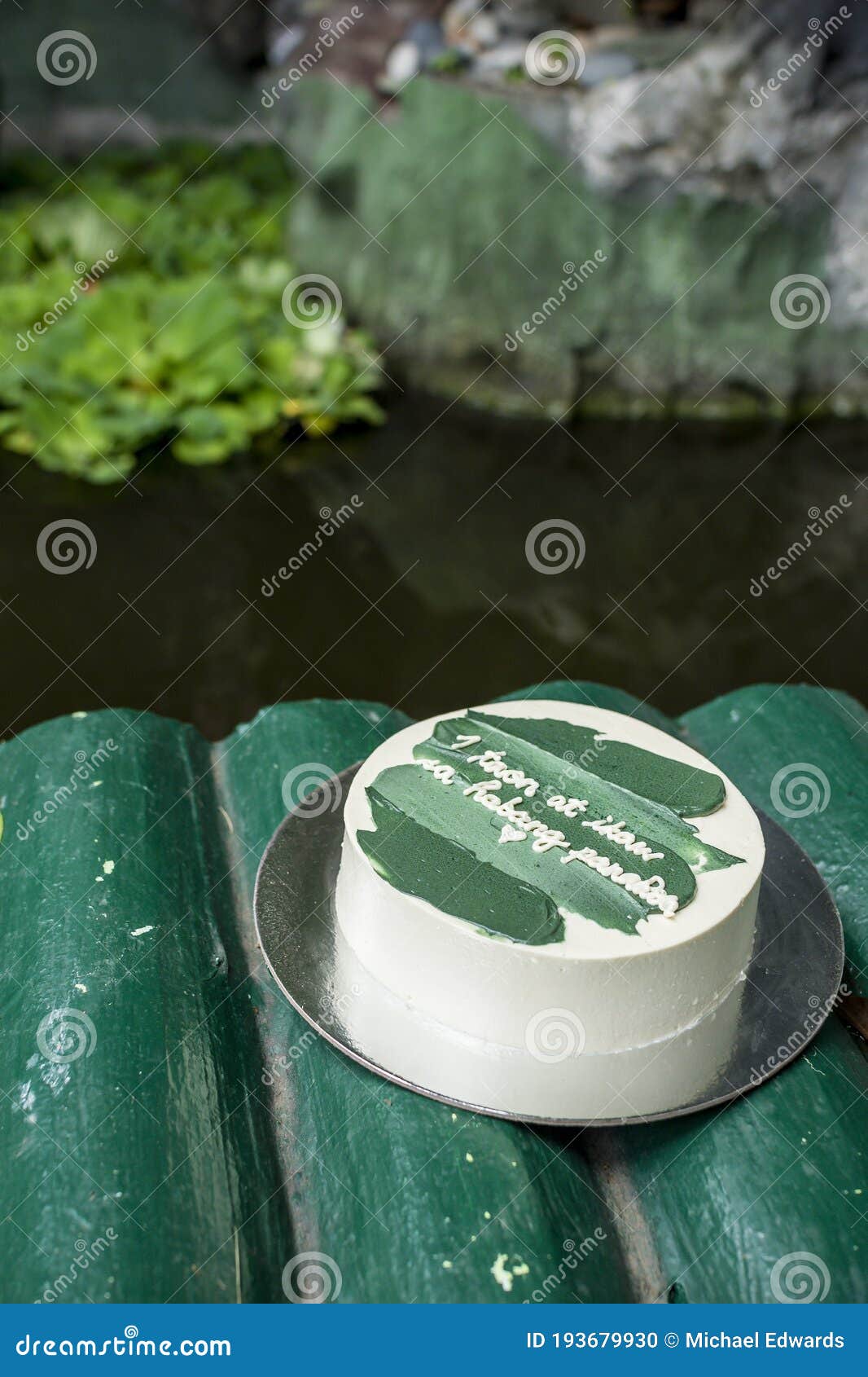 a small minimalist cake on a faux bamboo bridge by a koi pond. with tagalog words translated as 1 year and forever.