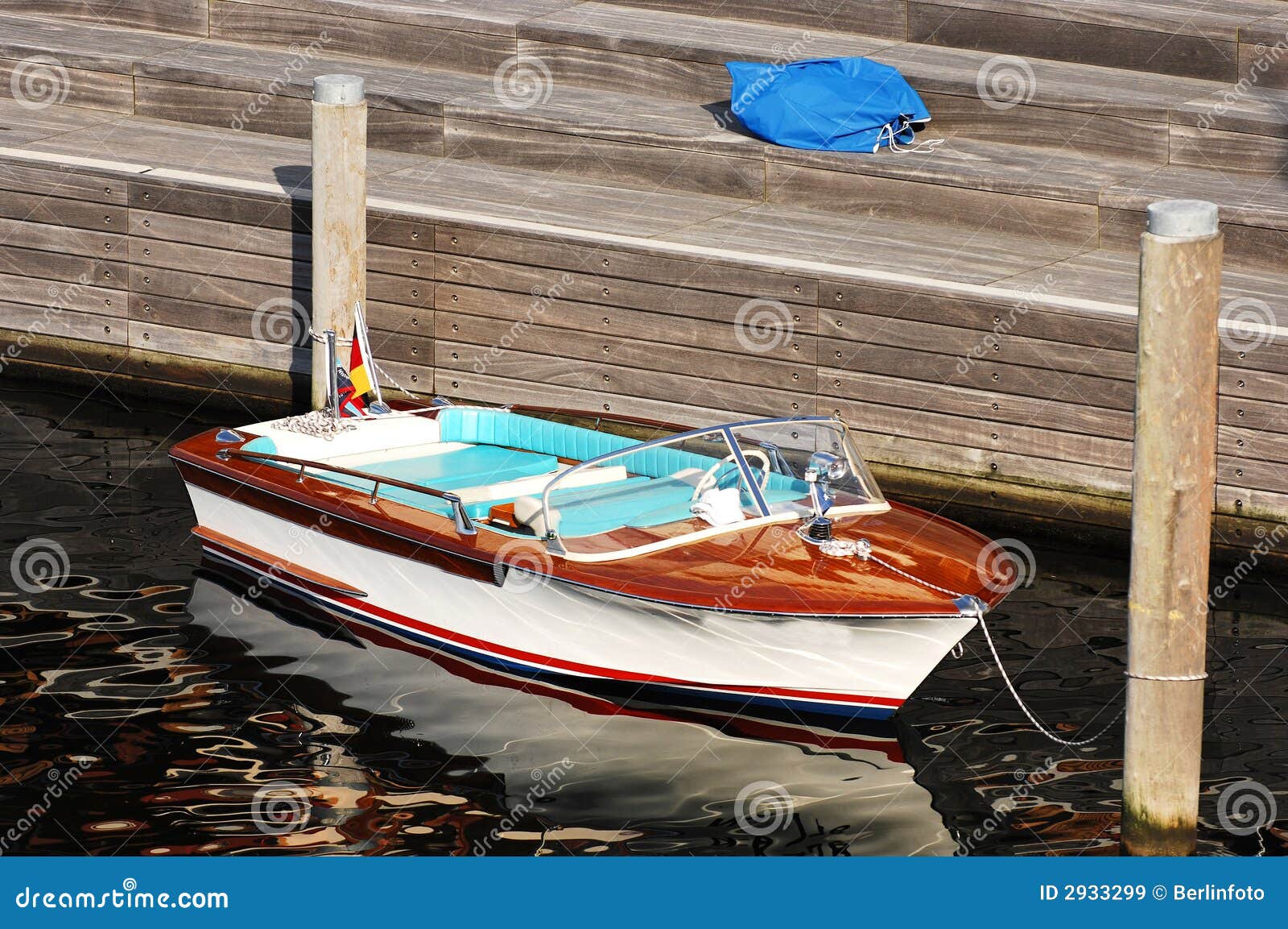 Small retro-style speed boat tied to large pier. Wooden planked dock 