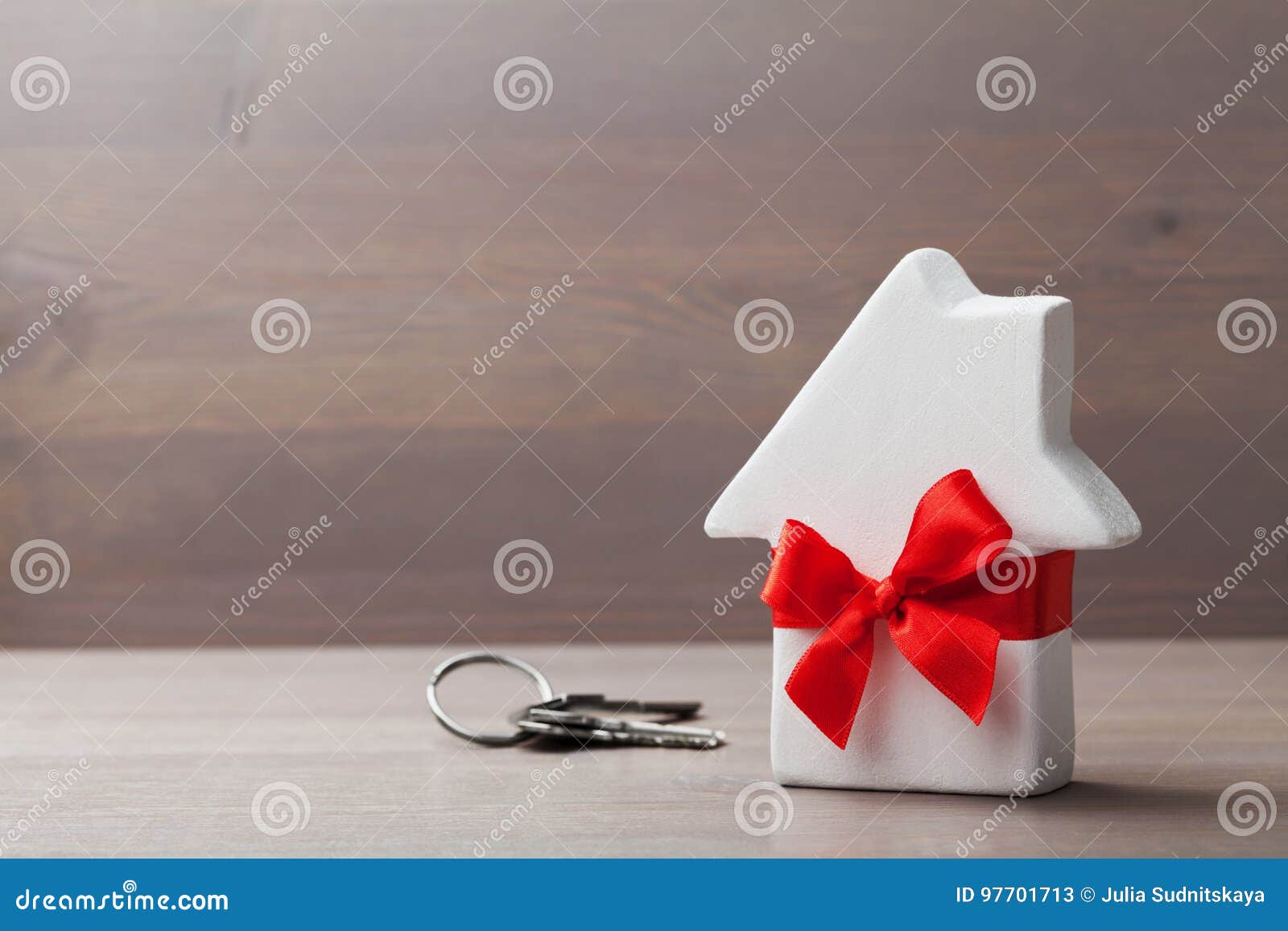 small white house decorated red bow ribbon with bunch of keys on wooden background. gift, real estate or buying a new home