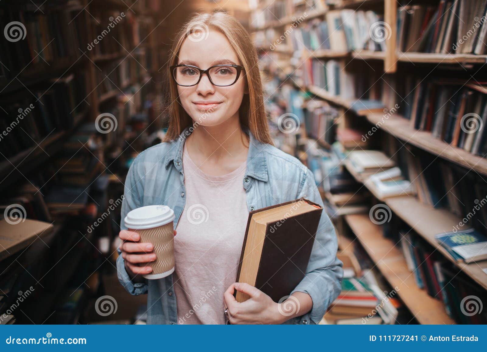 Smart And Clever Student Is Standing In The Public Library. She Is Holding A Cup Of ...
