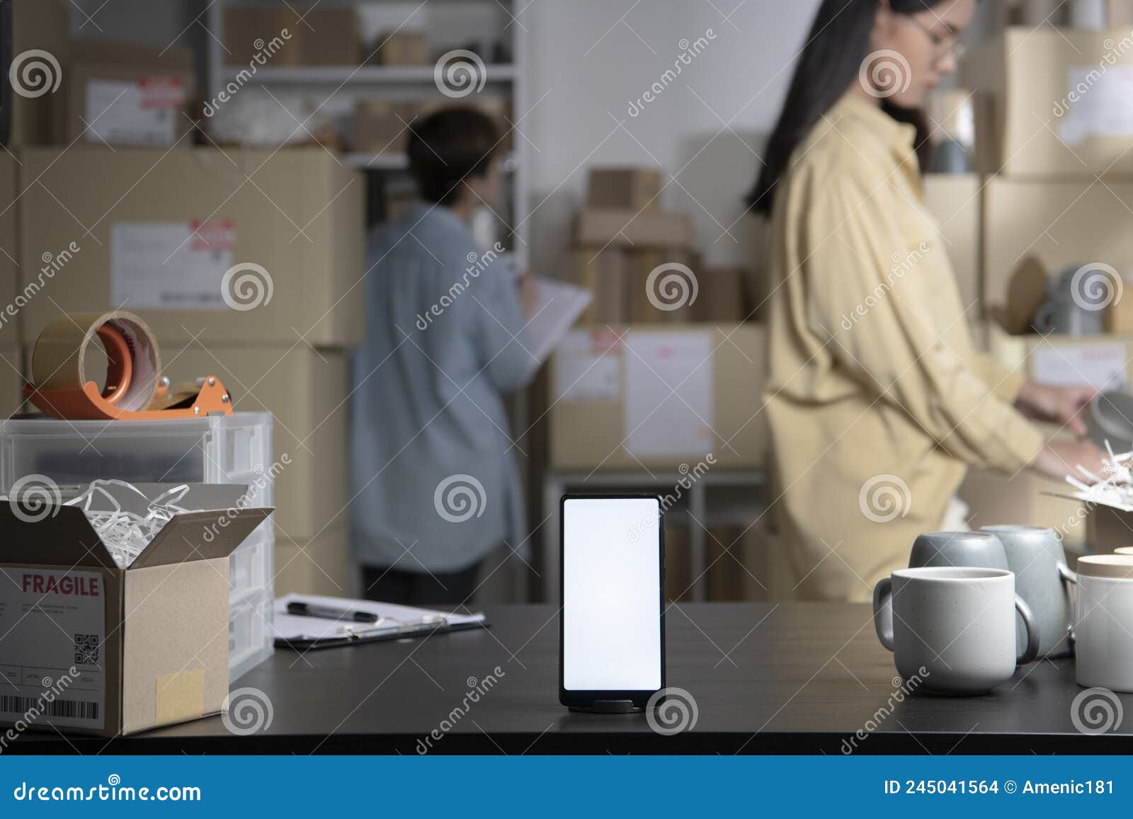 smartphone with blank white screen standing on the desktop in the warehouses. asian women online seller checking stock and invento
