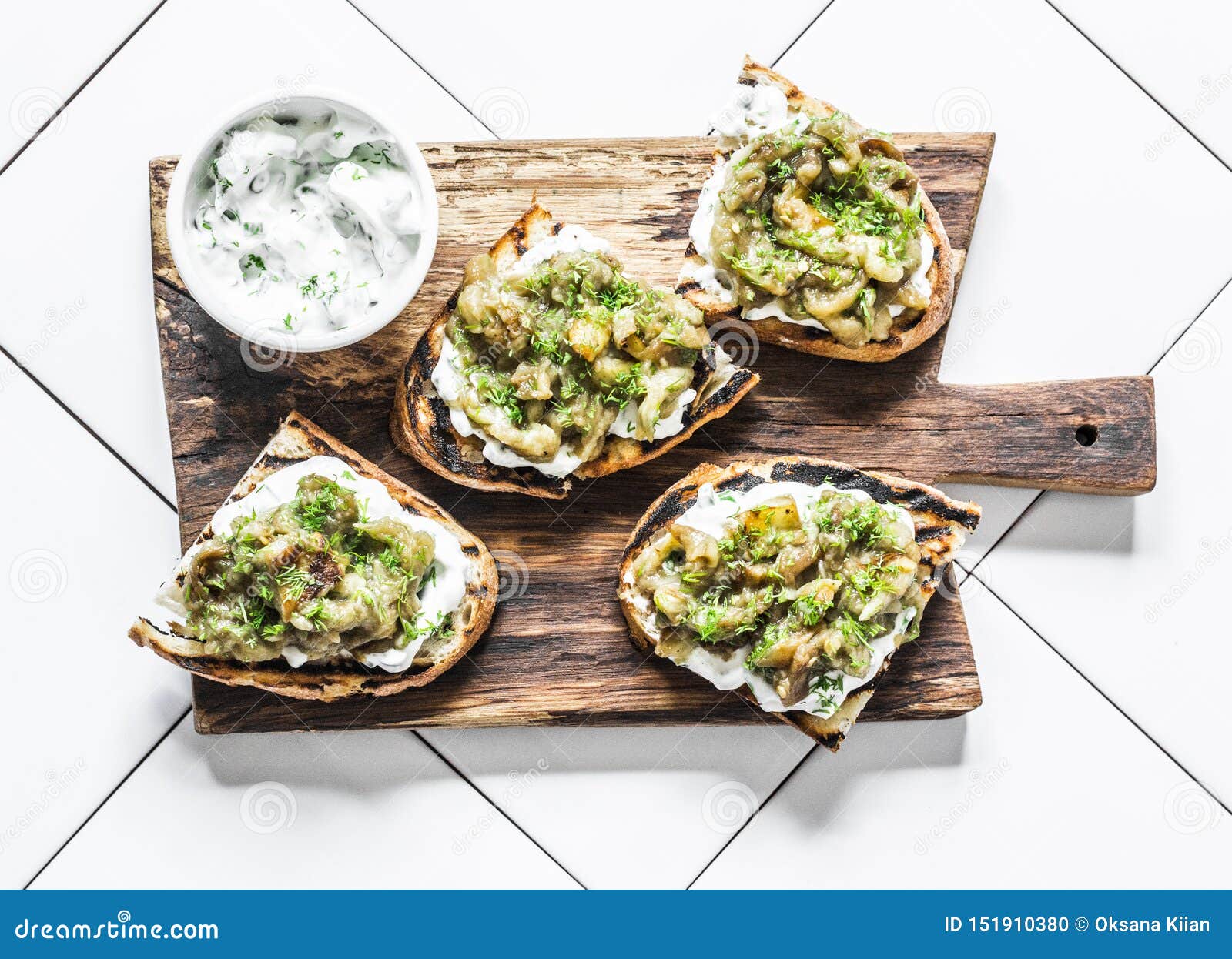 smashed grilled eggplant bruschetta with yogurt herbs sauce - delicious appetizers, snacks, tapas on cutting board on a light