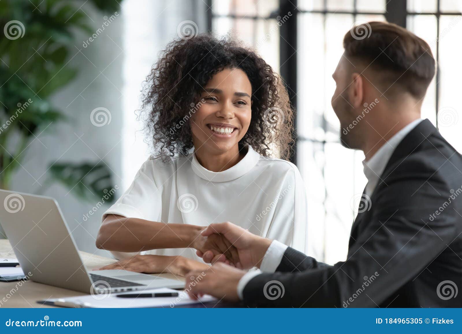 smiling african american businesswoman shaking client hand at meeting